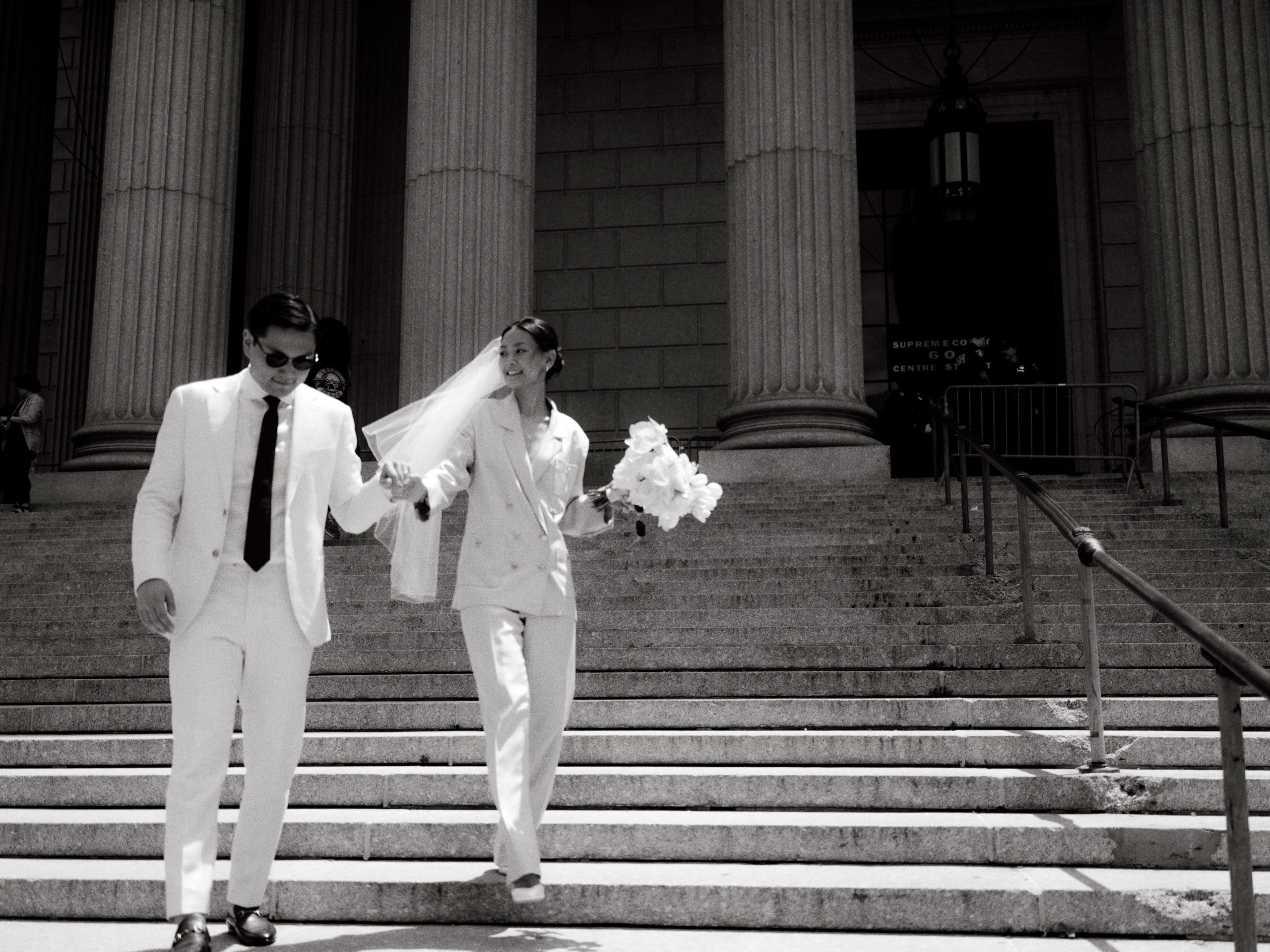The bride and groom are walking down the grand staircase of NYC City Hall. Editorial elopement image by Jenny Fu Studio.