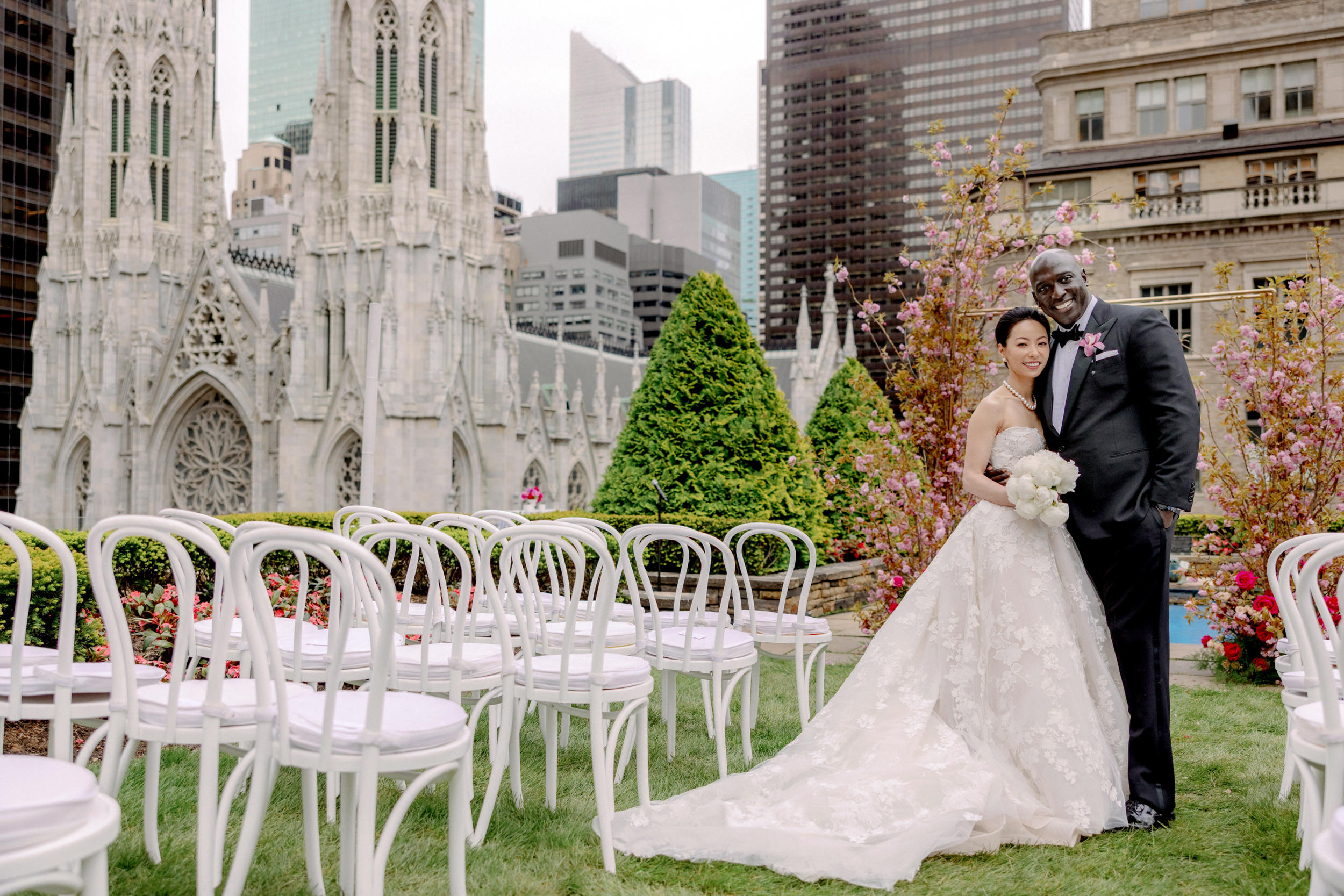 The bride and groom are smiling happily at 620 Loft & Garden, NYC, with the St. Patrick's Cathedral in the background. 