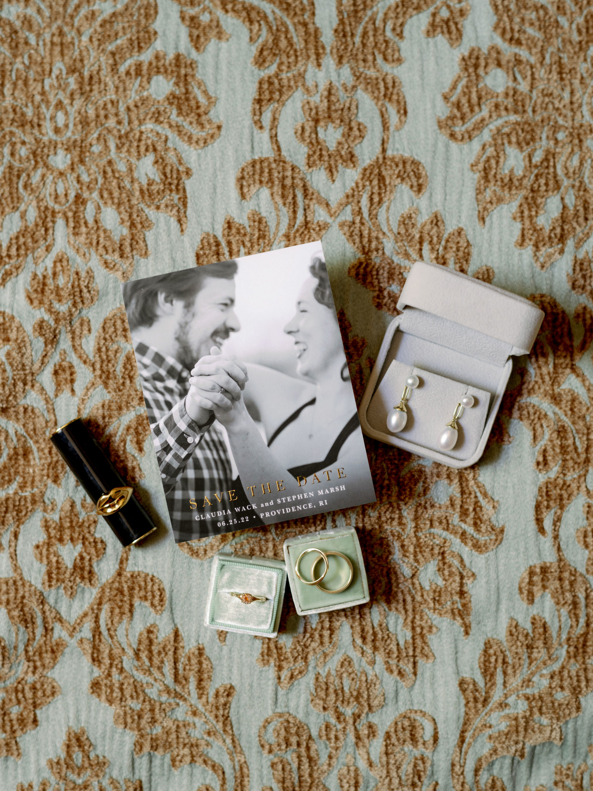 A save-the-date card with an engagement image printed on it, is placed on a table, together with wedding rings and accessories.