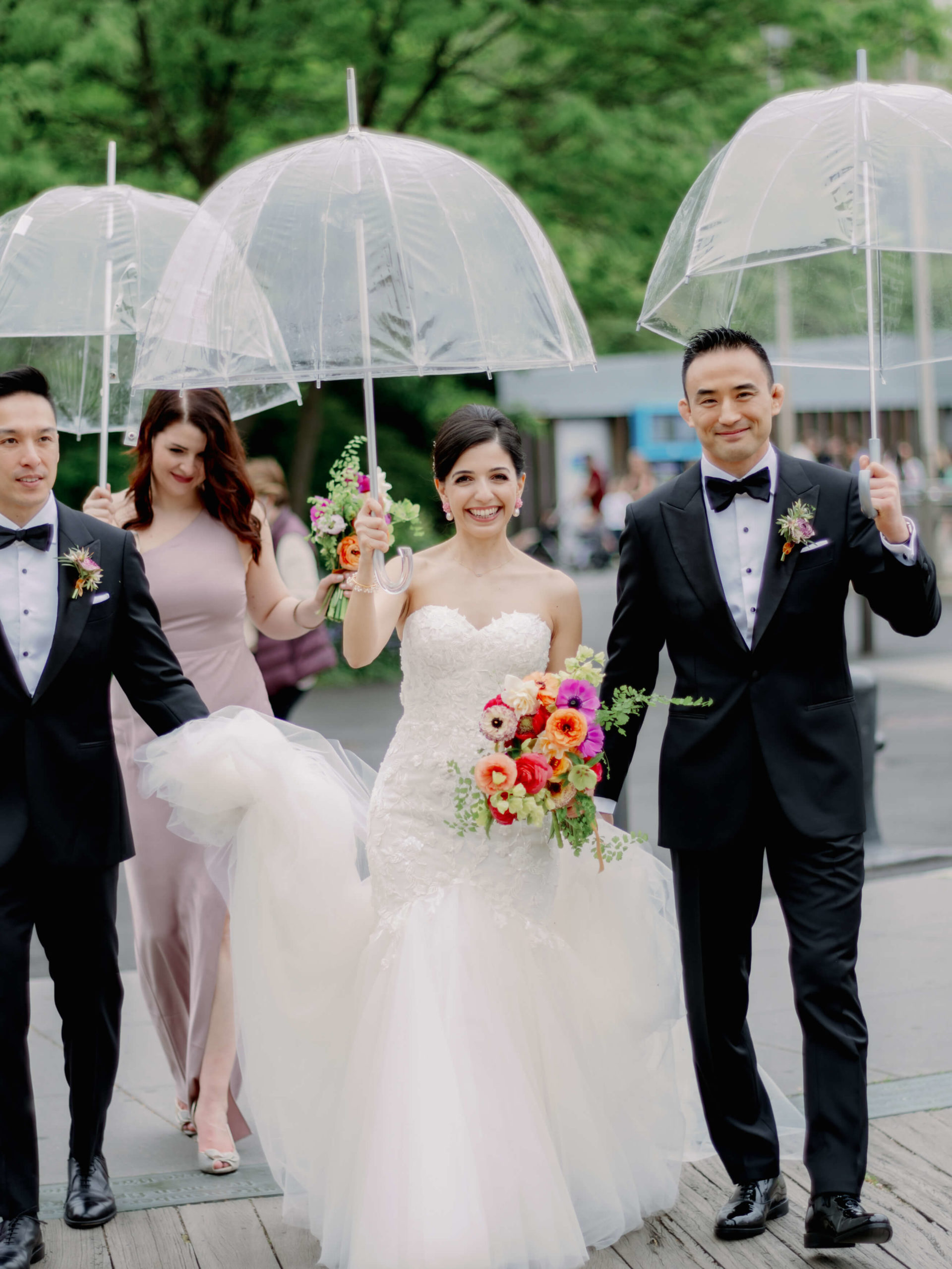 The bride and groom are walking in the street with transparent umbrellas. Editorial wedding image by Jenny Fu Studio