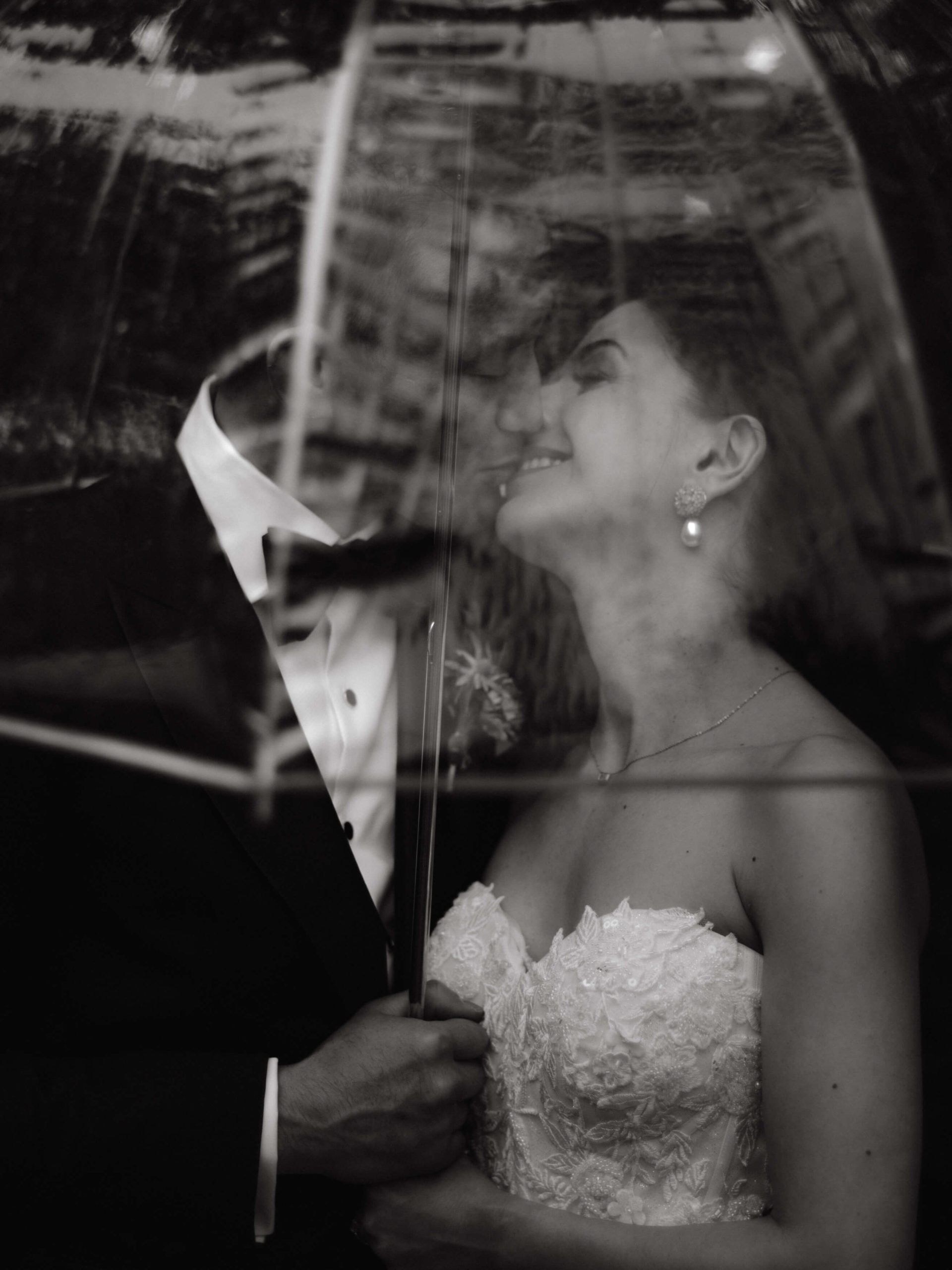 The newlywed couple is kissing underneath a transparent umbrella in NYC. Image by Jenny Fu Studio