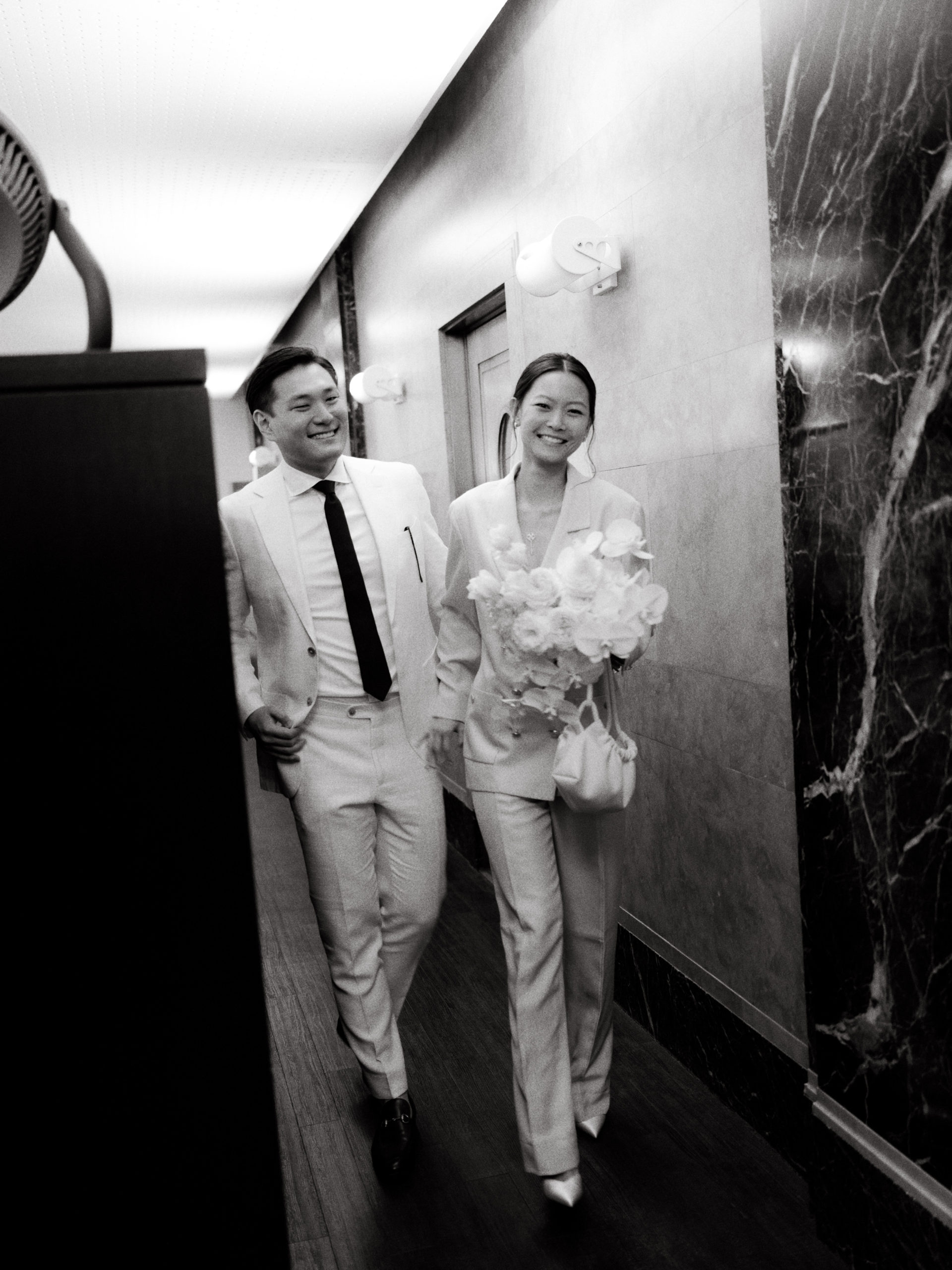 The newlyweds are walking in the hallway going to the exit door of NYC Marriage Bureau. Personalized NYC City Hall wedding image by Jenny Fu Studio
