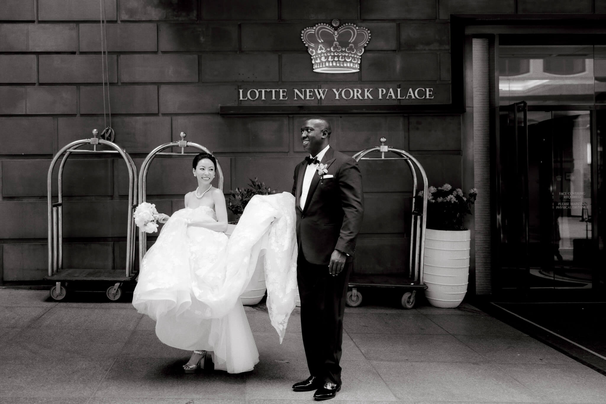 Black and white image of the bride and groom exiting Lotte New York Palace. Image by Jenny Fu Studio