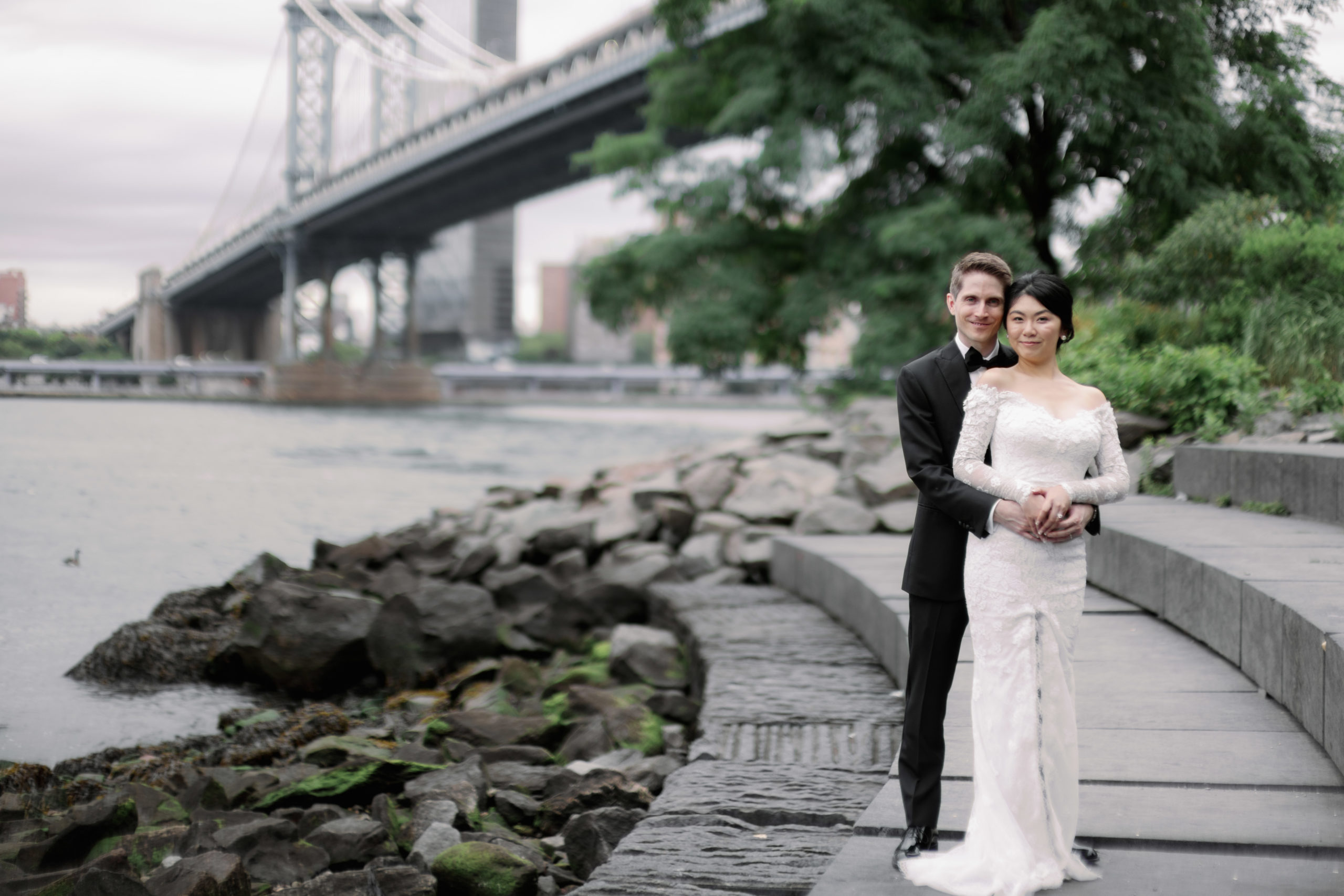 The newlyweds are standing in Brooklyn Bridge Park with the Brooklyn Bridge in the background. Image by Jenny Fu Studio