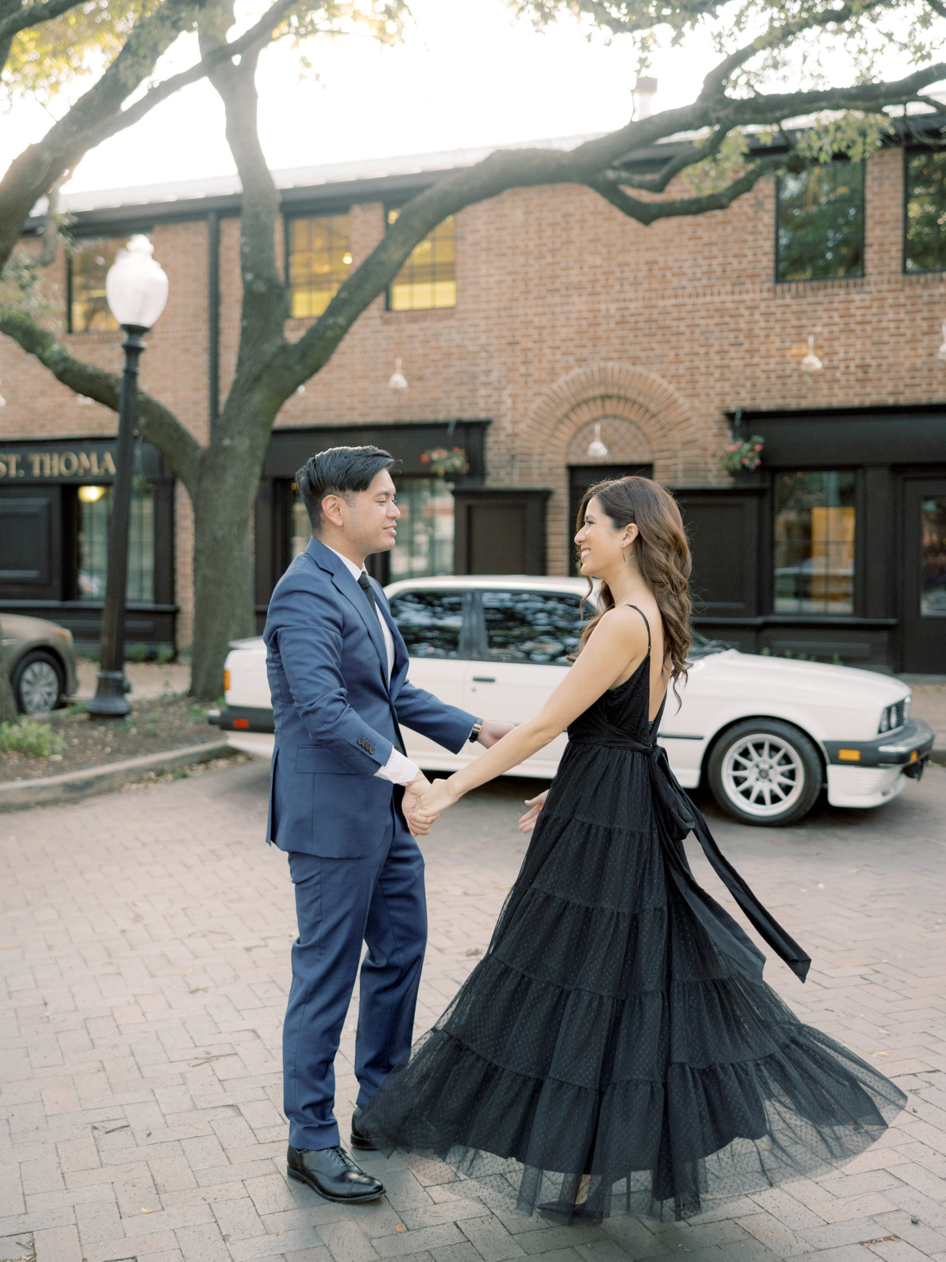 The engaged couple are holding hands while happily looking at each other in front of a red brick building. Engagement photos by Jenny Fu Studio 