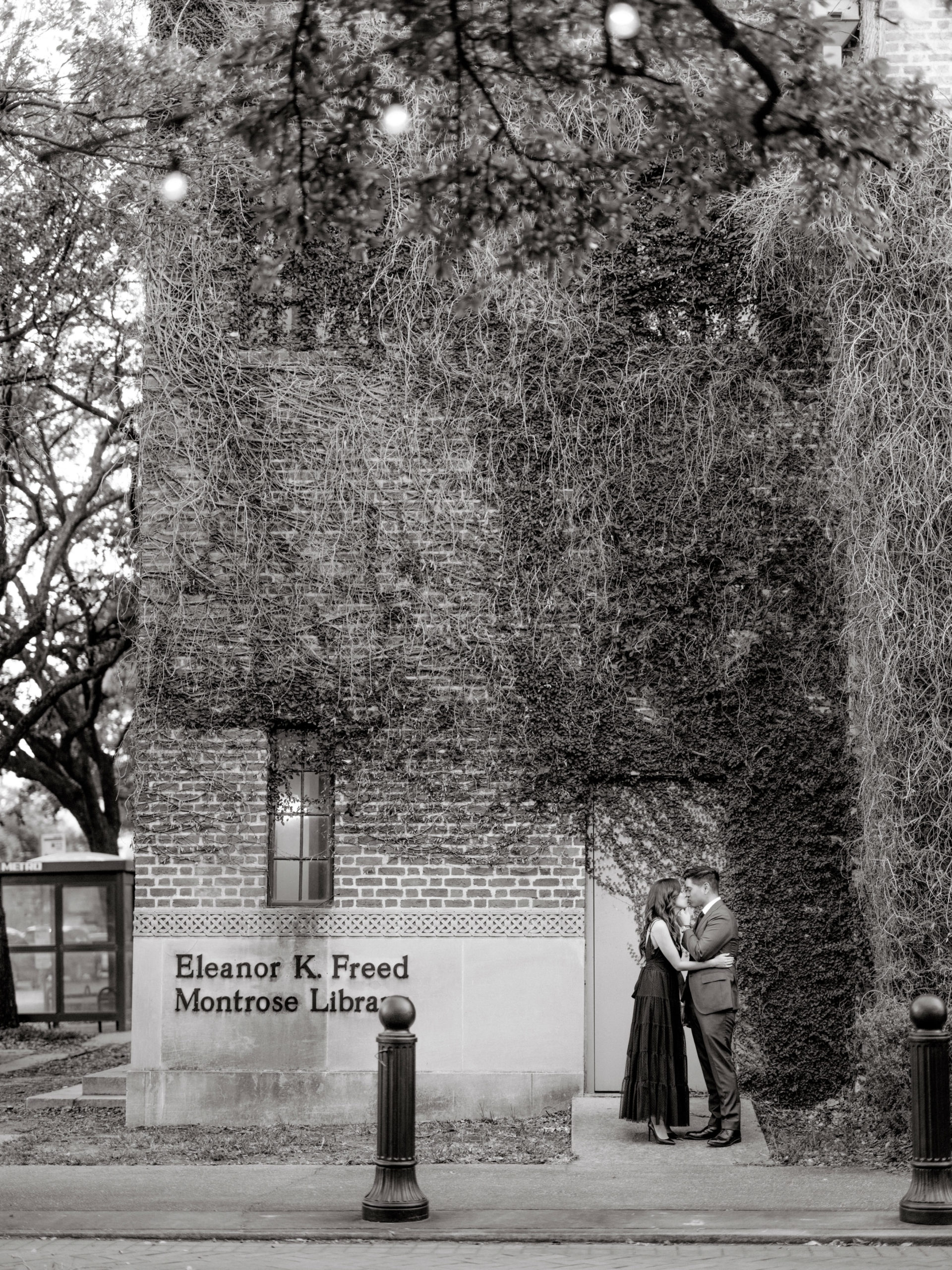 Black and white photo of the engaged couple kissing in front of Eleanor K. Freed Montrose Library. Professional Engagement photos by Jenny Fu Studio