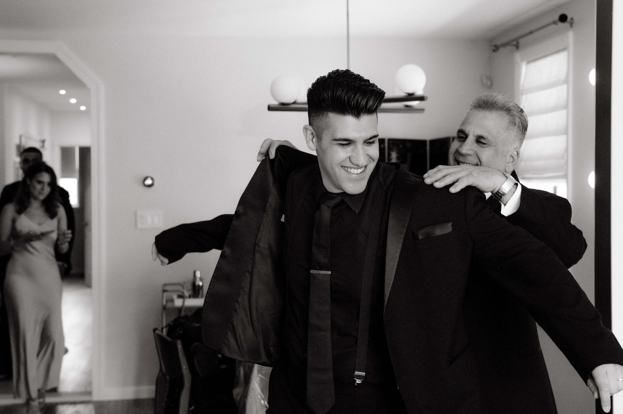 Black and white photo of the groom and father putting on his coat. Image by Jenny Fu Studio