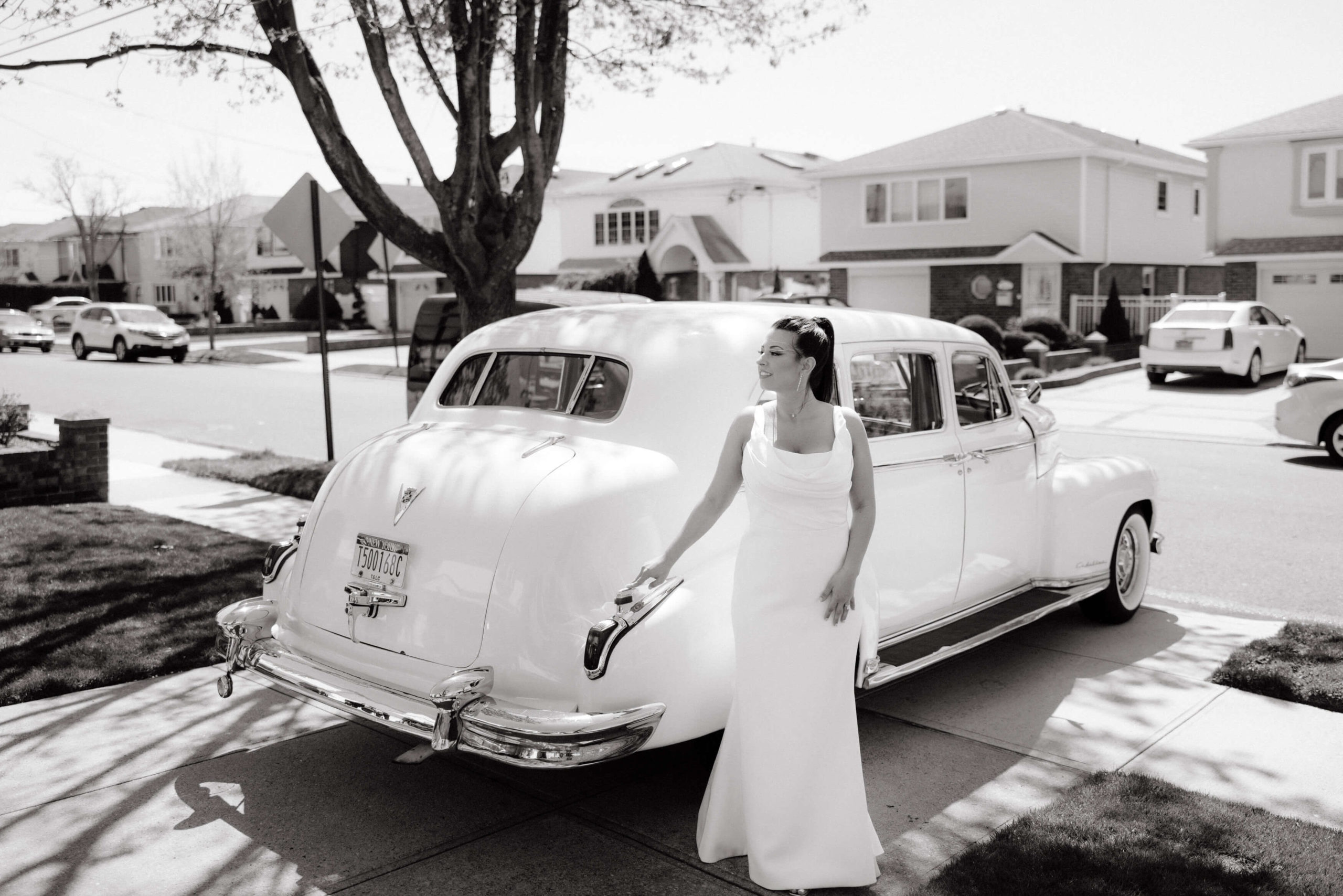 Black and white photo of the bride posing in front of a white old school luxury car. Image by Jenny Fu Studio