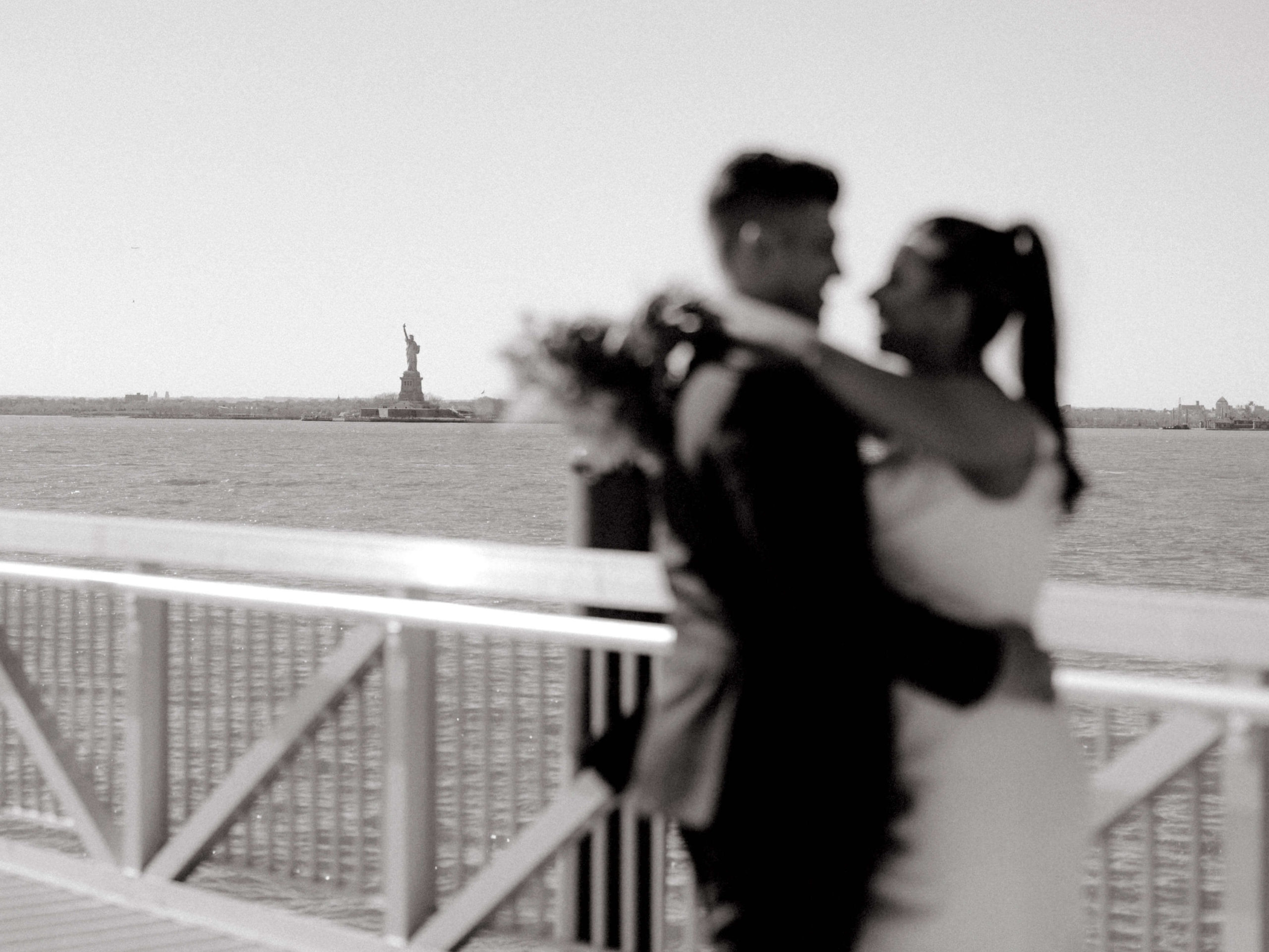 Editorial photo of the married couple hugging each other with the Statue of Liberty in the background. Image by Jenny Fu Studio