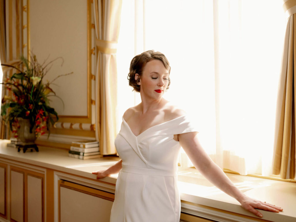 bride looking and feeling beautiful after makeup and hair on her wedding day standing by window