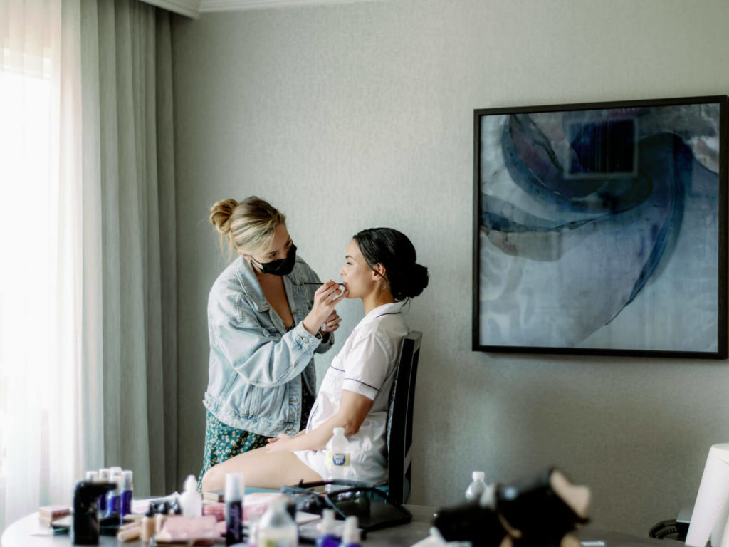 bride getting makeup done with makeup artist placing lip color with a brush on her wedding day