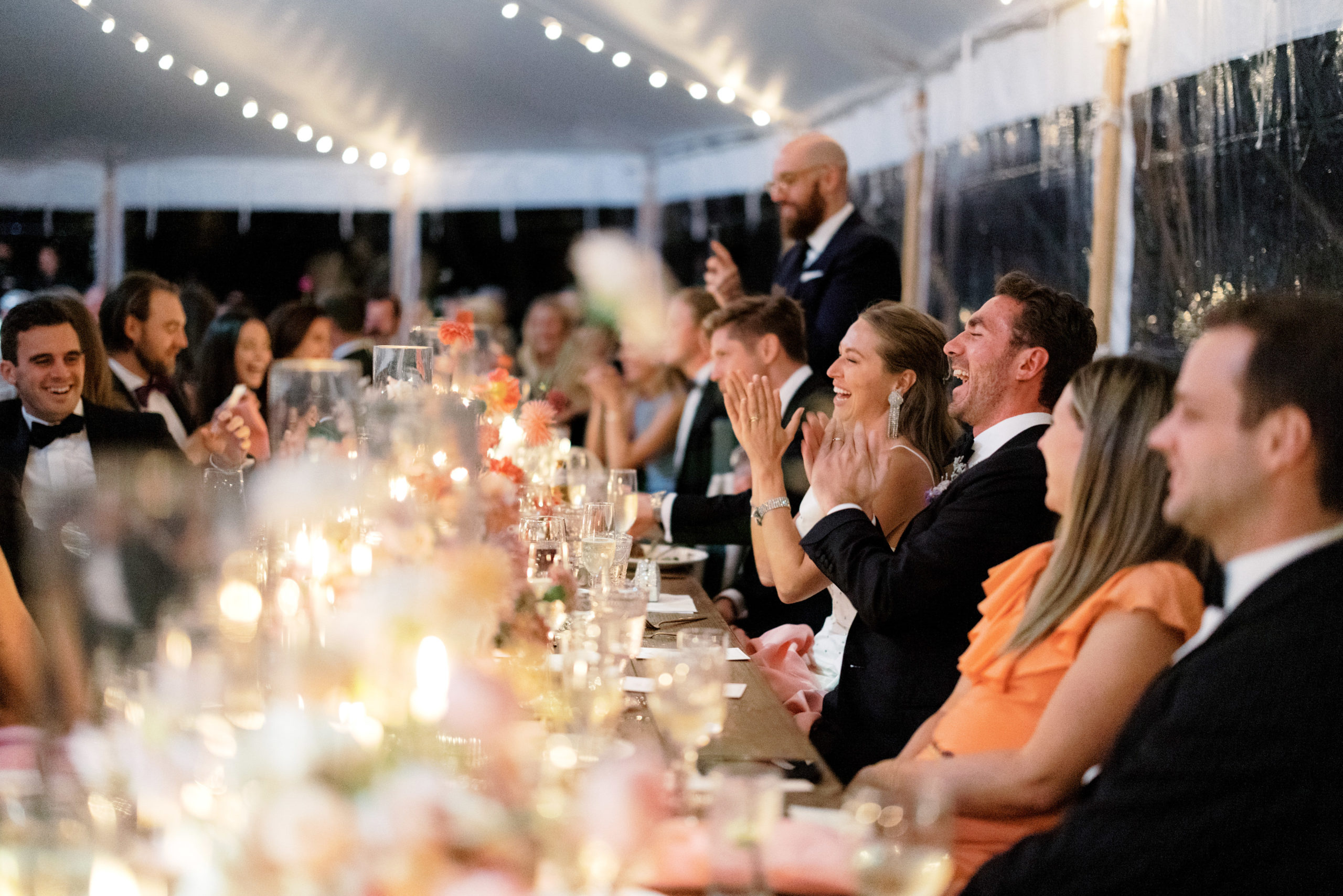 The bride, groom and wedding guests are laughing at the dining table at the Ausable Club, NY. Image by Jenny Fu Studio