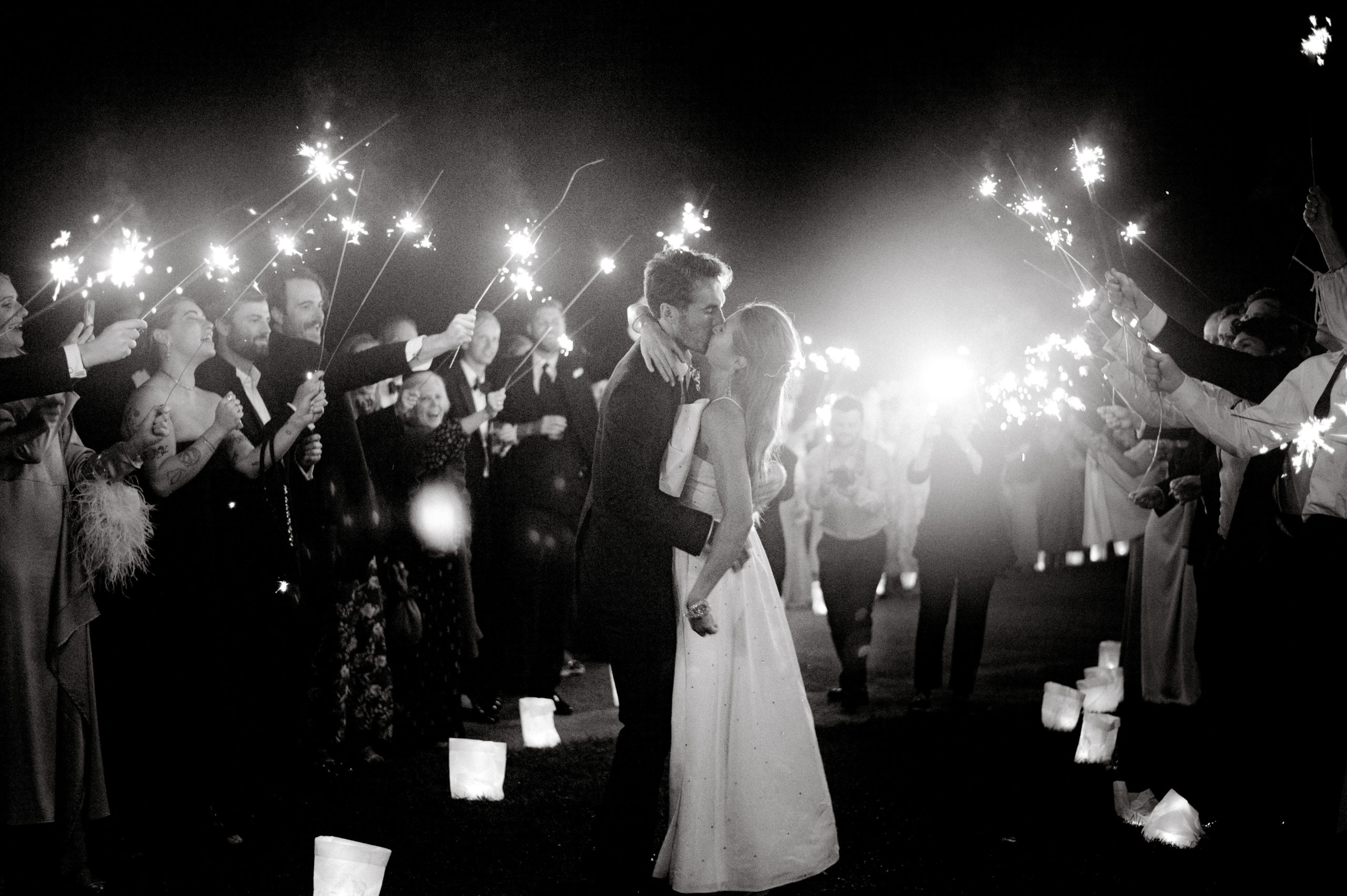 Black and white image of the bride and groom kissing  with sparklers in the background at the Ausable Club, NY. Image by Jenny Fu Studio