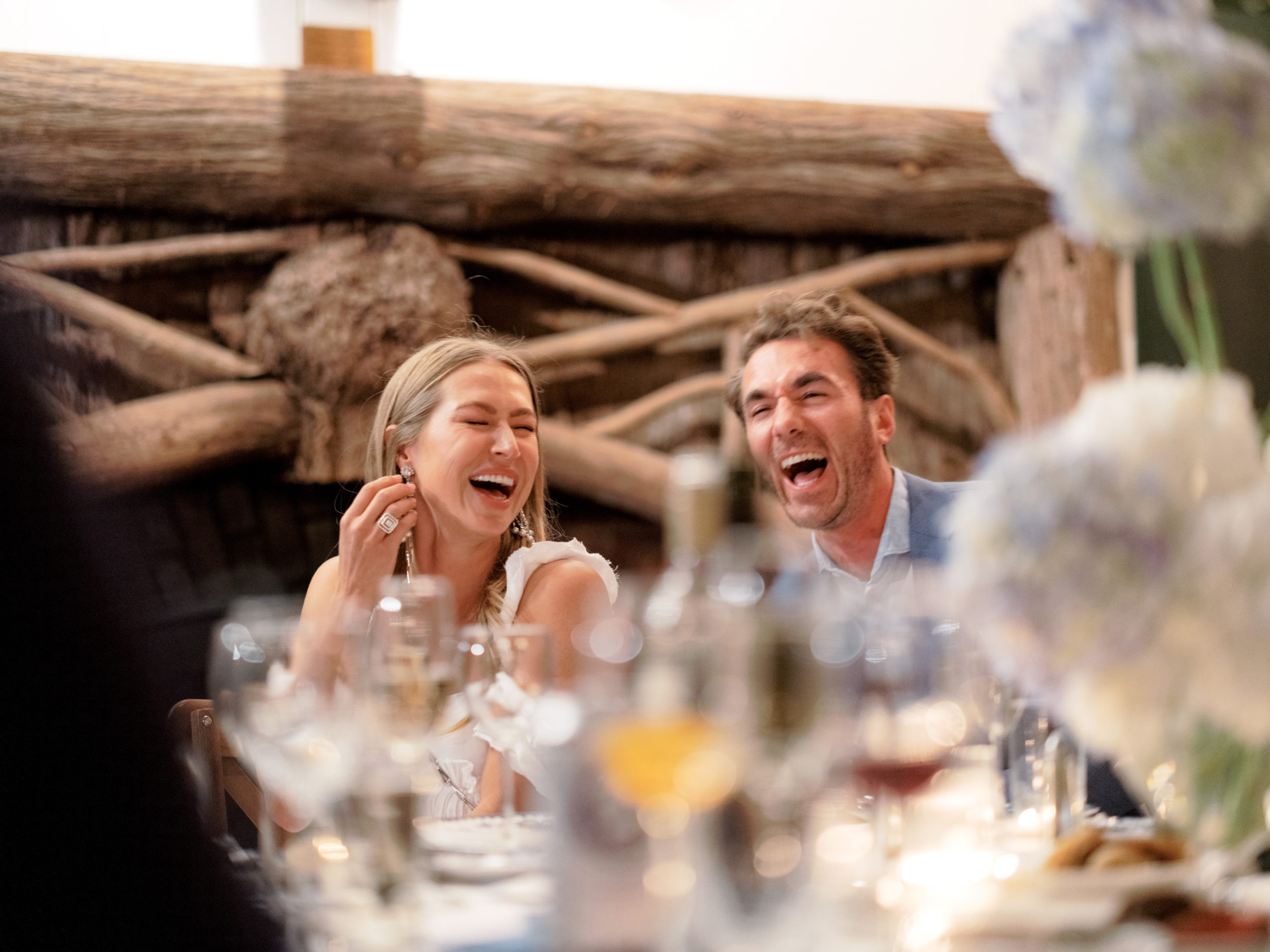 The bride and groom-to-be  are laughing in a welcome dinner at The Ausable Club NY. Image by Jenny Fu Studio