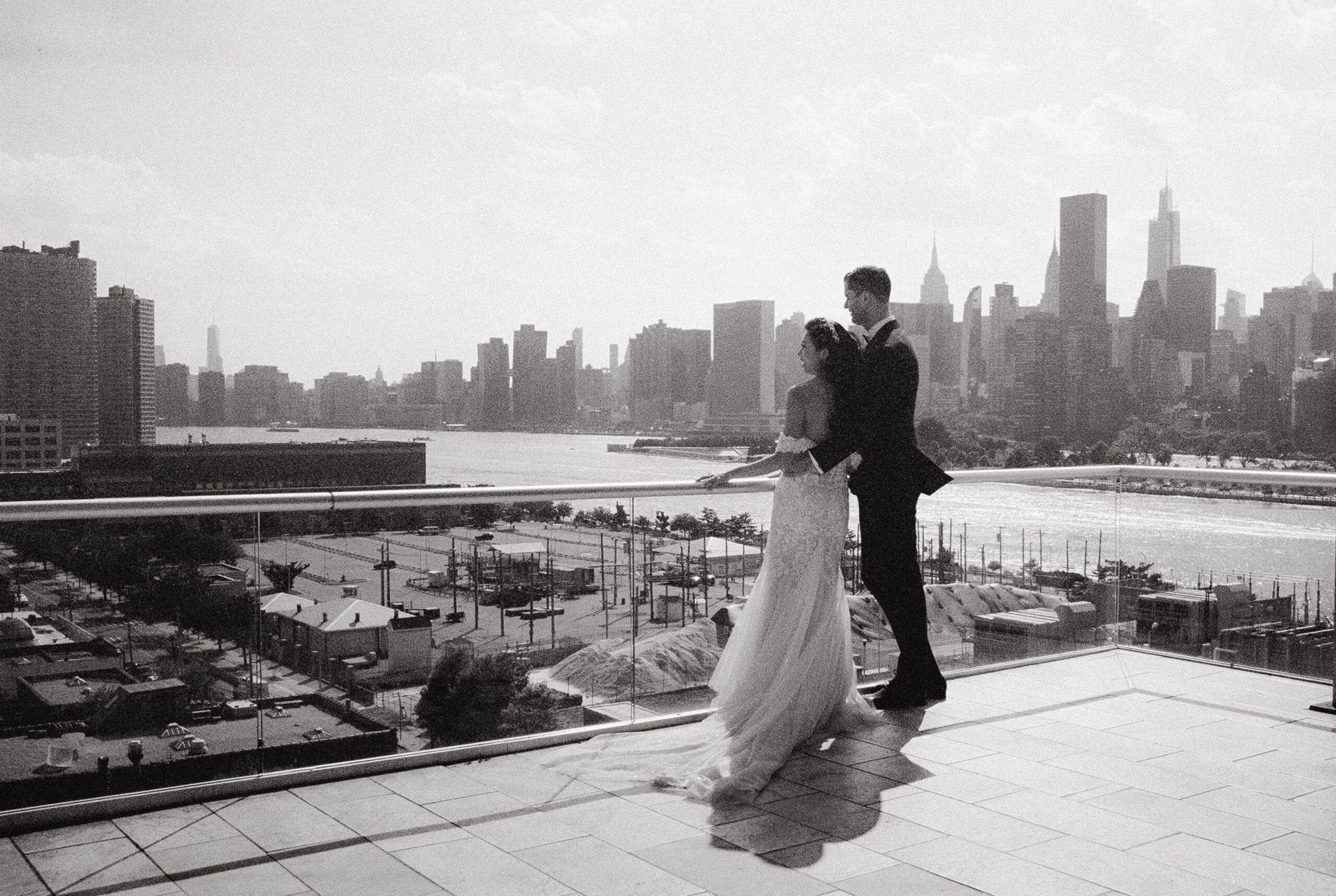 Black and white photo of the newlyweds with the NYC skyscrapers in the background. Film wedding photography image by Jenny Fu Studio