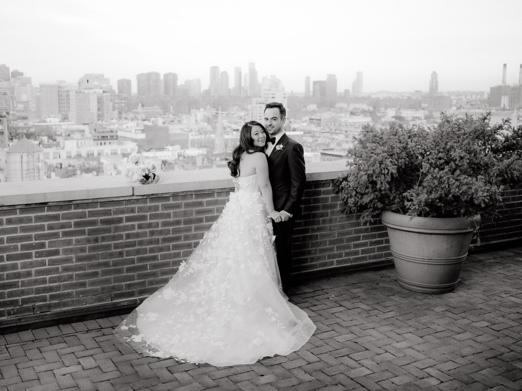 Black and white image of the bride and groom hugging each other with NYC skyscrapers in the background. Image by Jenny Fu Studio