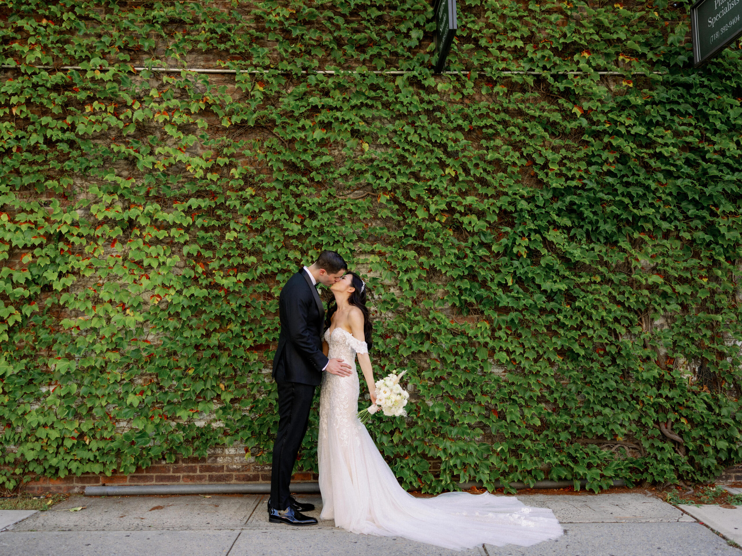 The bride and groom are kissing with ivy-covered wall in the background. Image by Jenny Fu Studio 