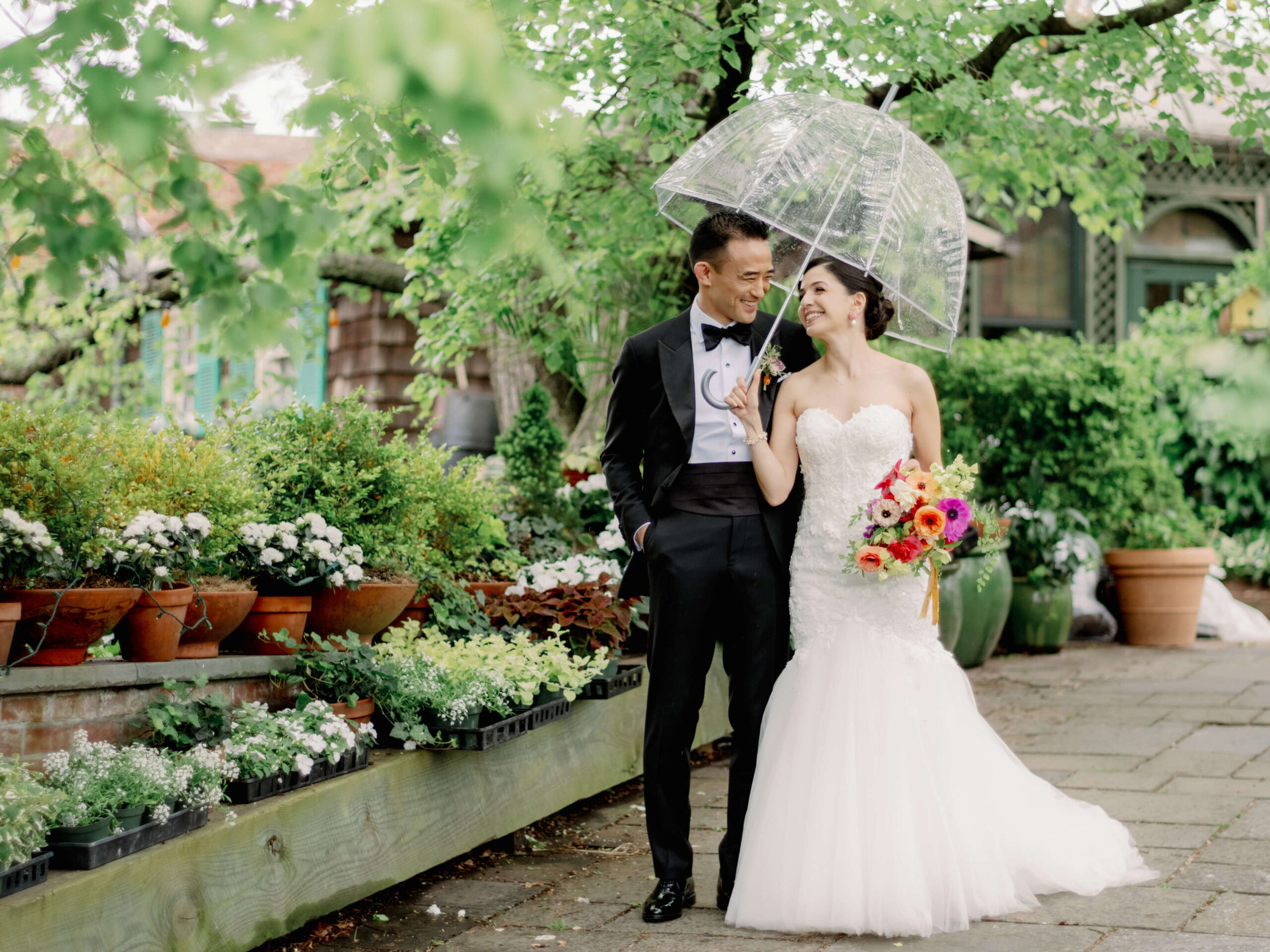 The bride and groom are walking outdoors under a clear umbrella. Image by Jenny Fu Studio