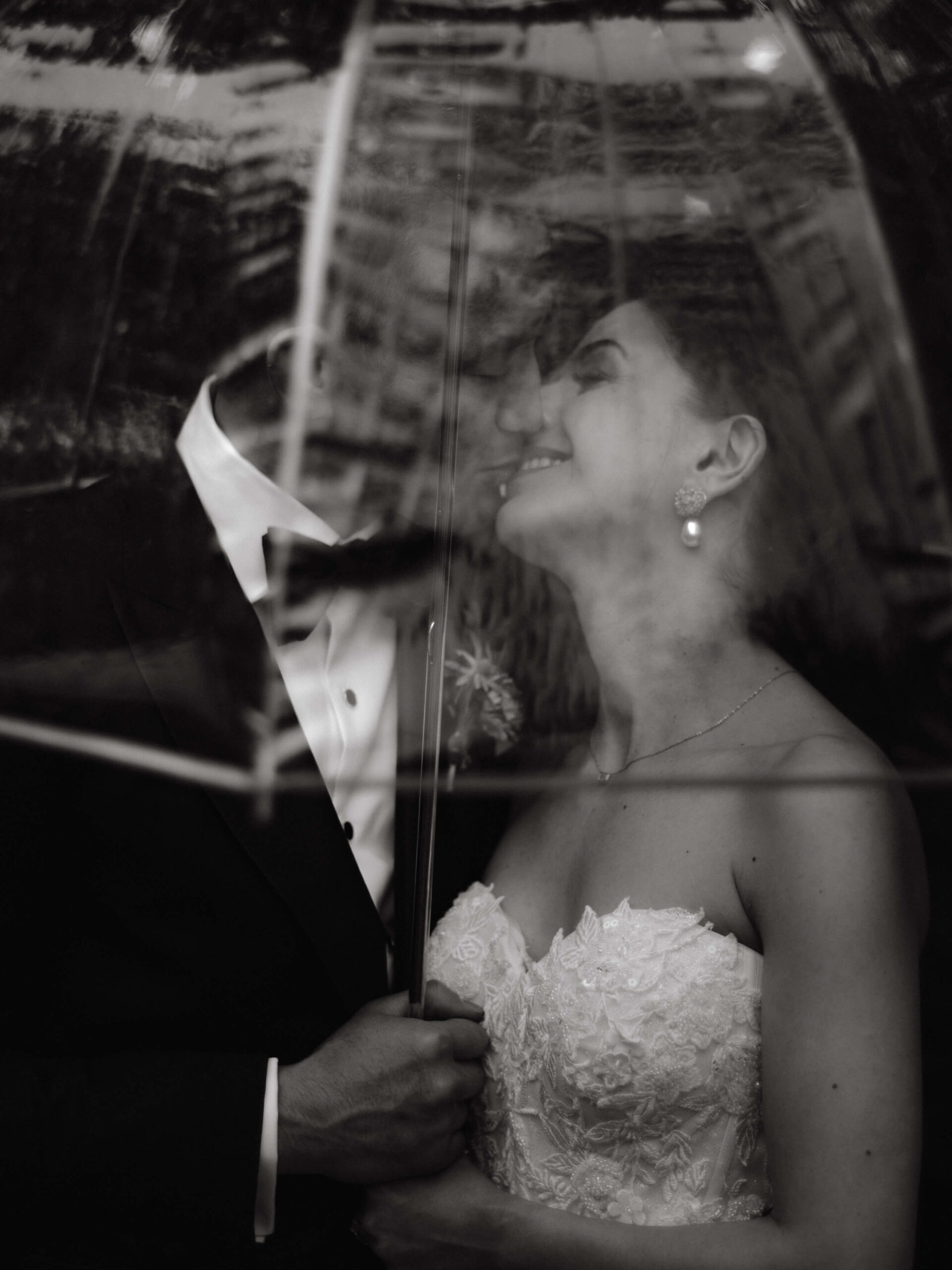 Black and white image of the bride and groom kissing under a clear umbrella. Image by Jenny Fu Studio