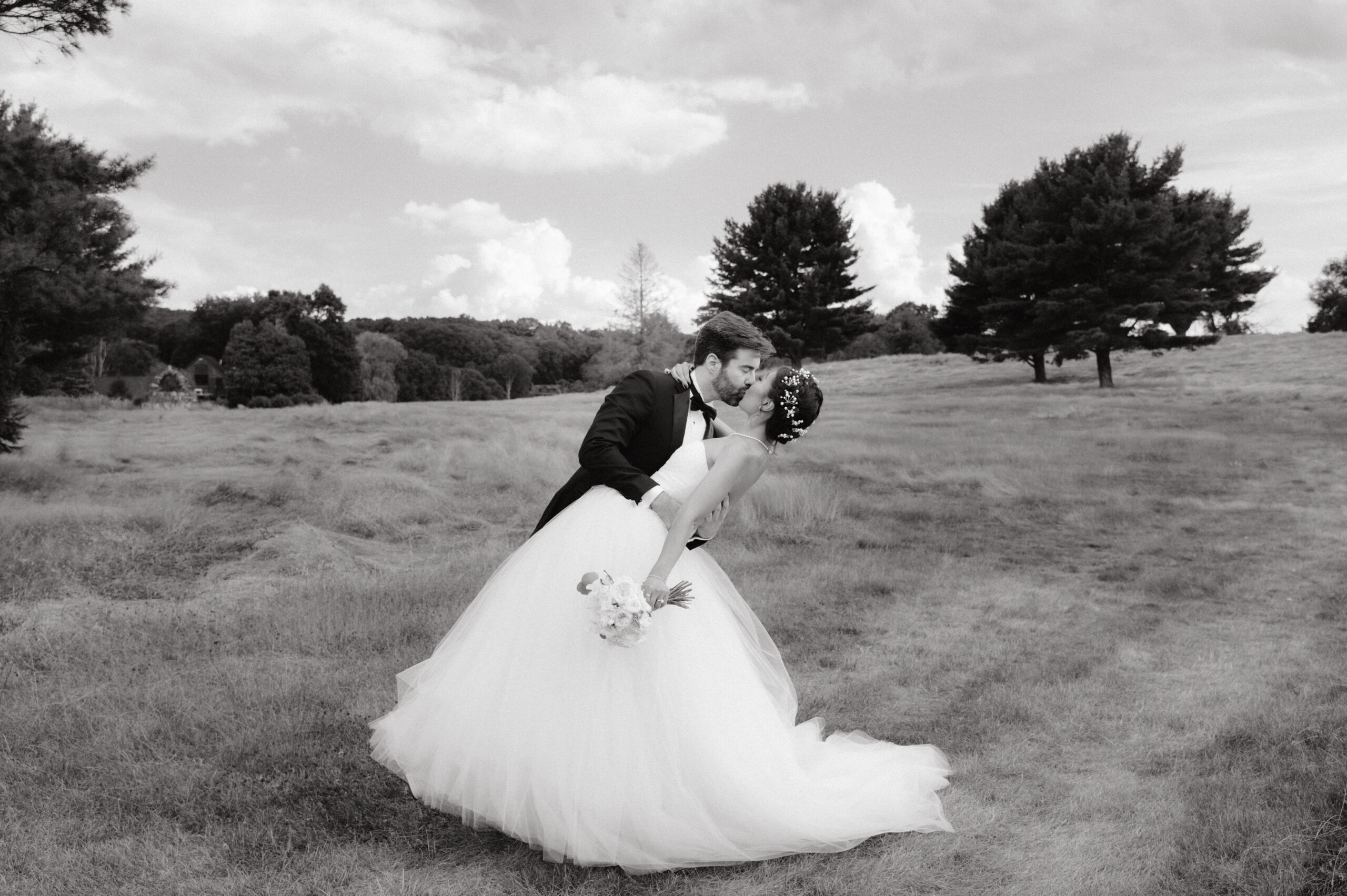 Black and white first look photo of the bride and groom, kissing in an open field. Image by Jenny Fu Studio 