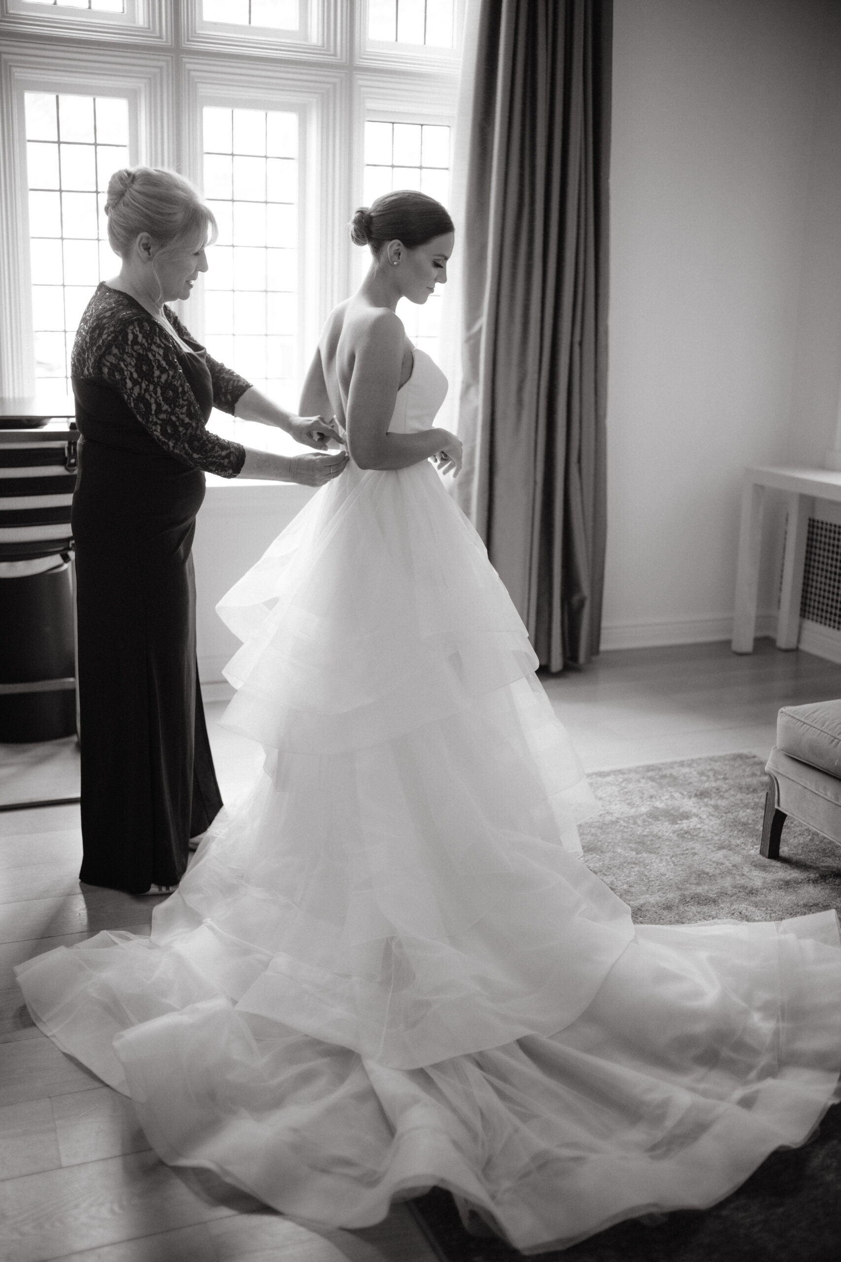 Editorial photo of the mother of the bride buttoning her daughter's wedding dress. Image by Jenny fu Studio