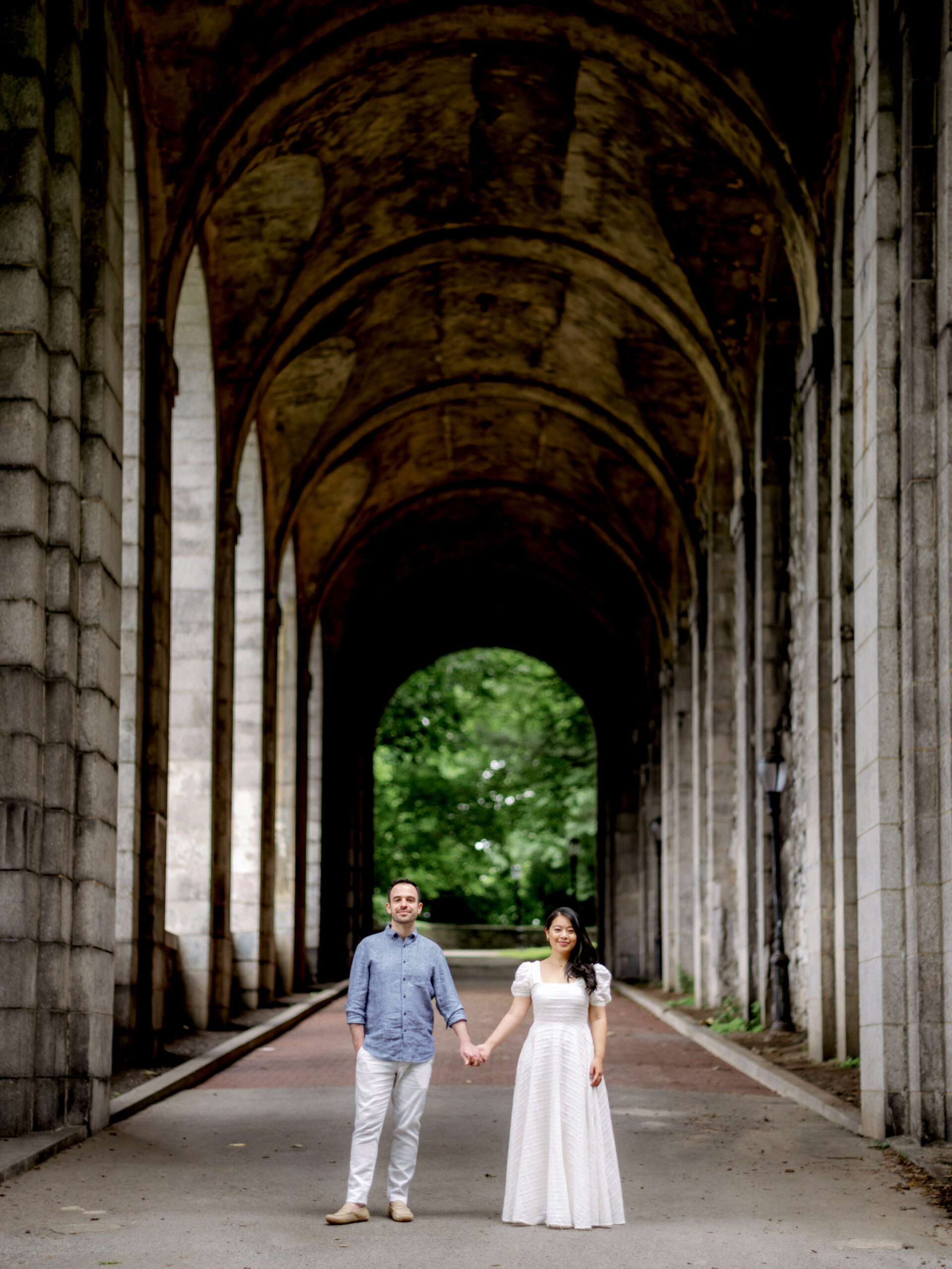 The engaged couple are standing side-by-side while holding hands with an old NYC building in the background. Engagement photos image by Jenny Fu Studio
