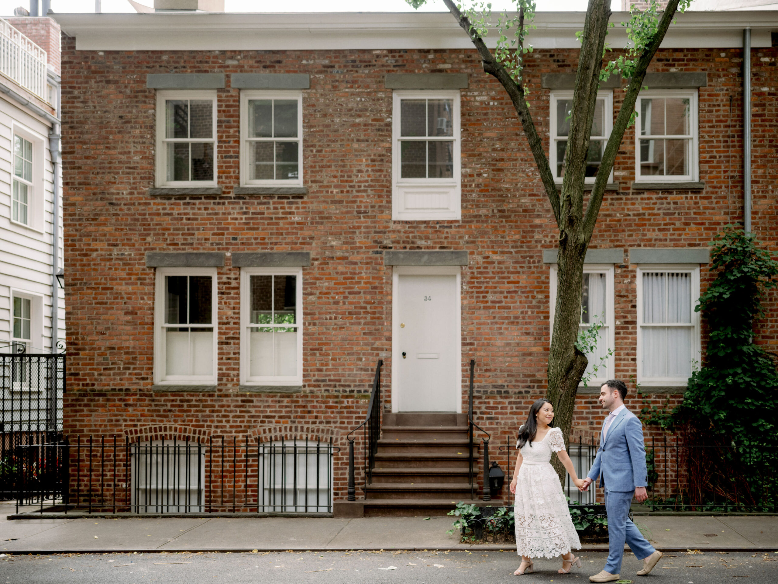 The engaged couple are walking the streets of NY with a red brick house in the background. Image by Jenny Fu Studio