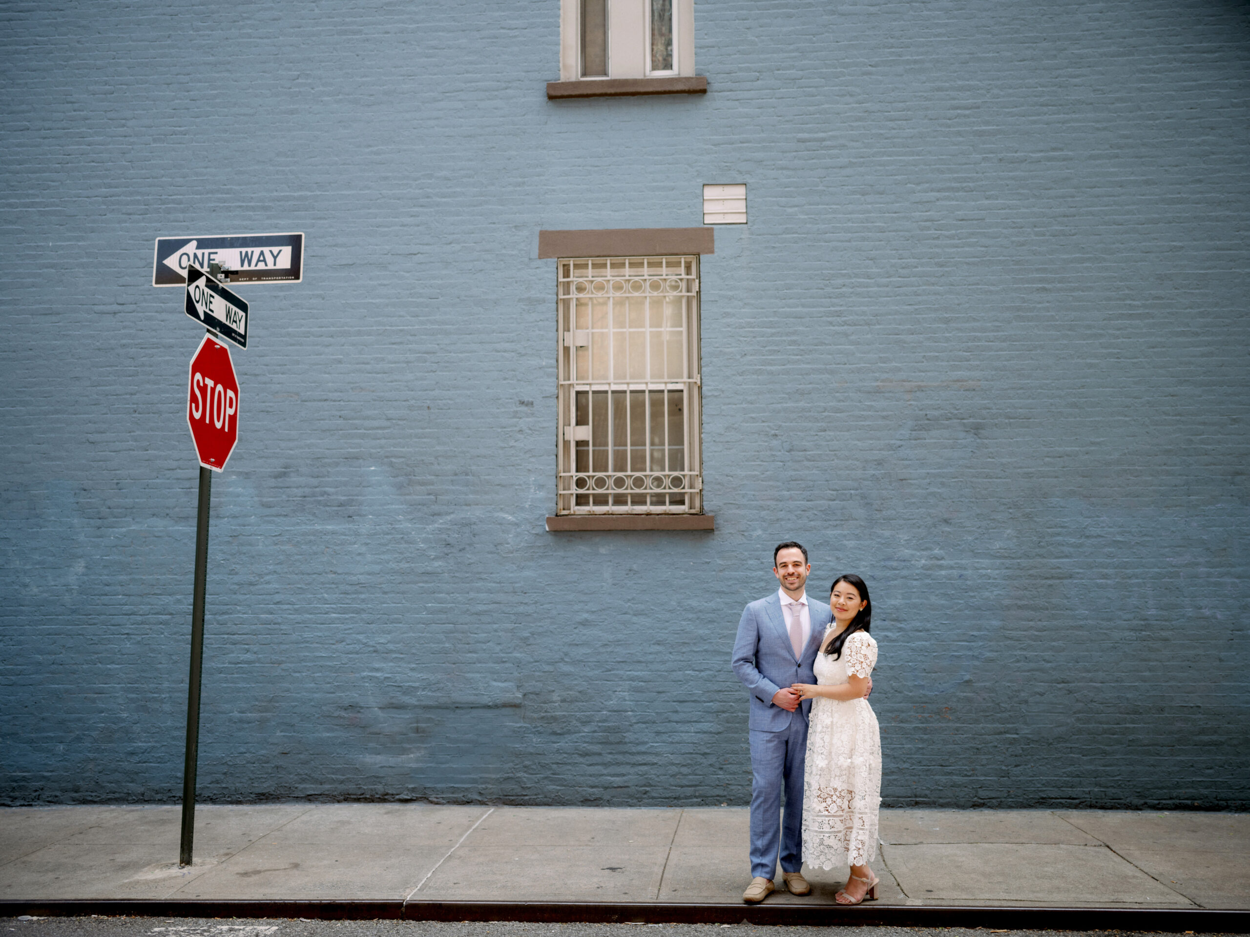 The engaged couple are standing with a blue building in the background in New York City. Engagement photos Image by Jenny Fu Studio