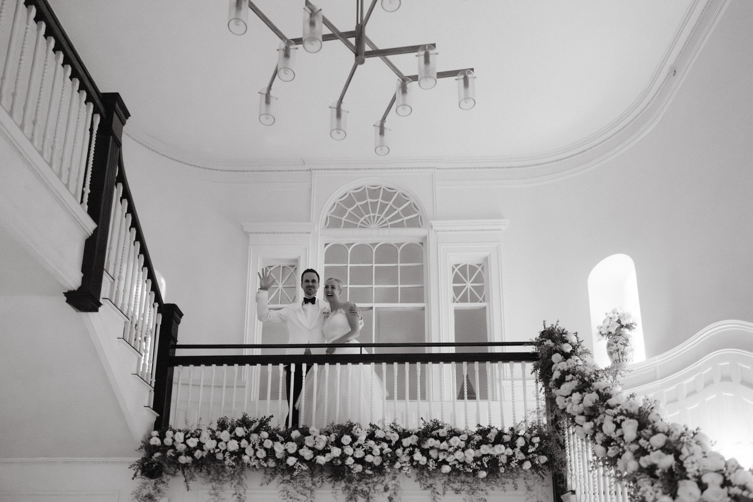 Black and white photo of the smiling bride and groom on top of the staircase filled with flowers. Wedding photography wish list photo by Jenny Fu Studio