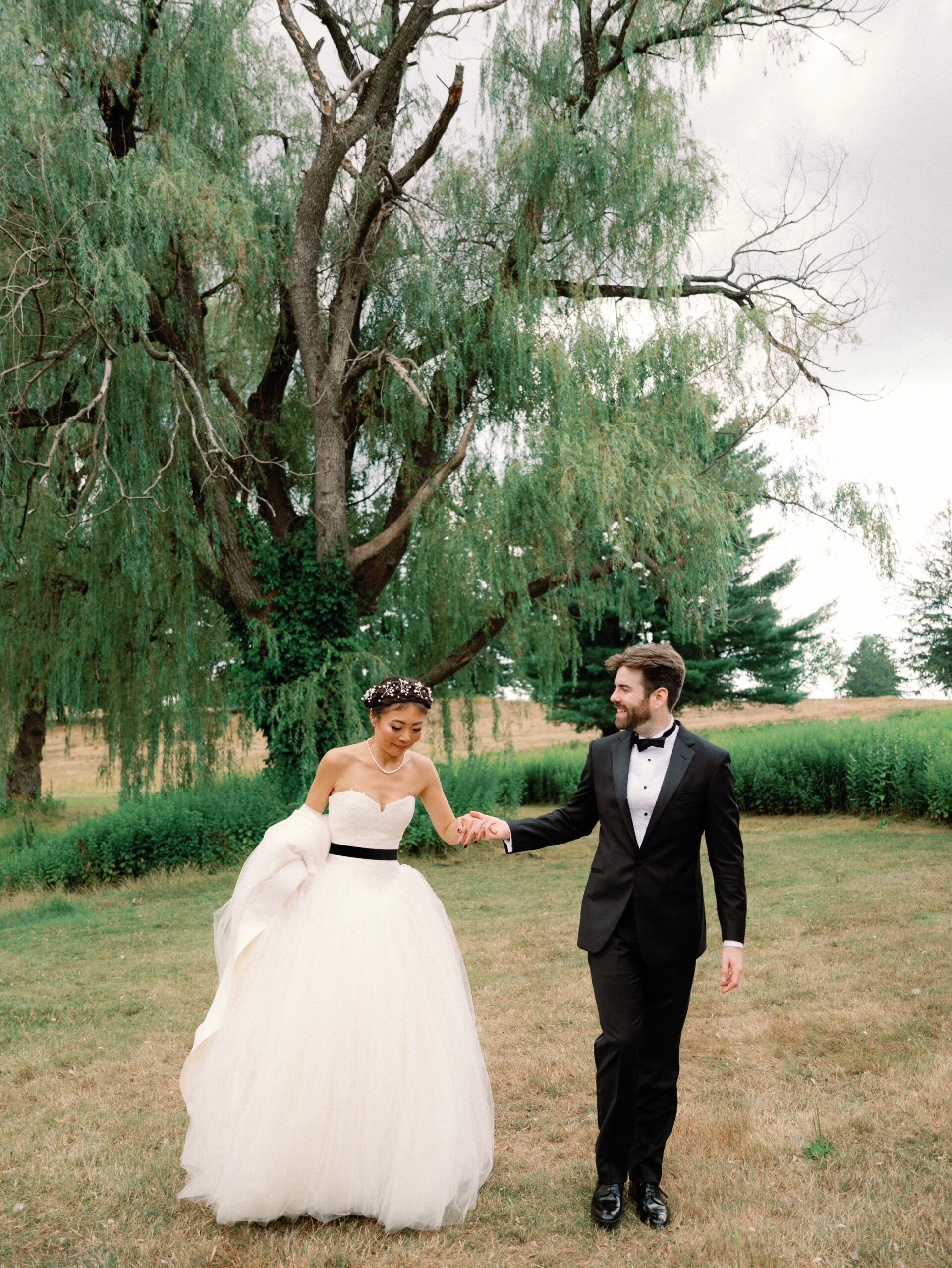 The bride and groom are walking outdoors with trees in the background. Wedding Personal style image by Jenny Fu Studio