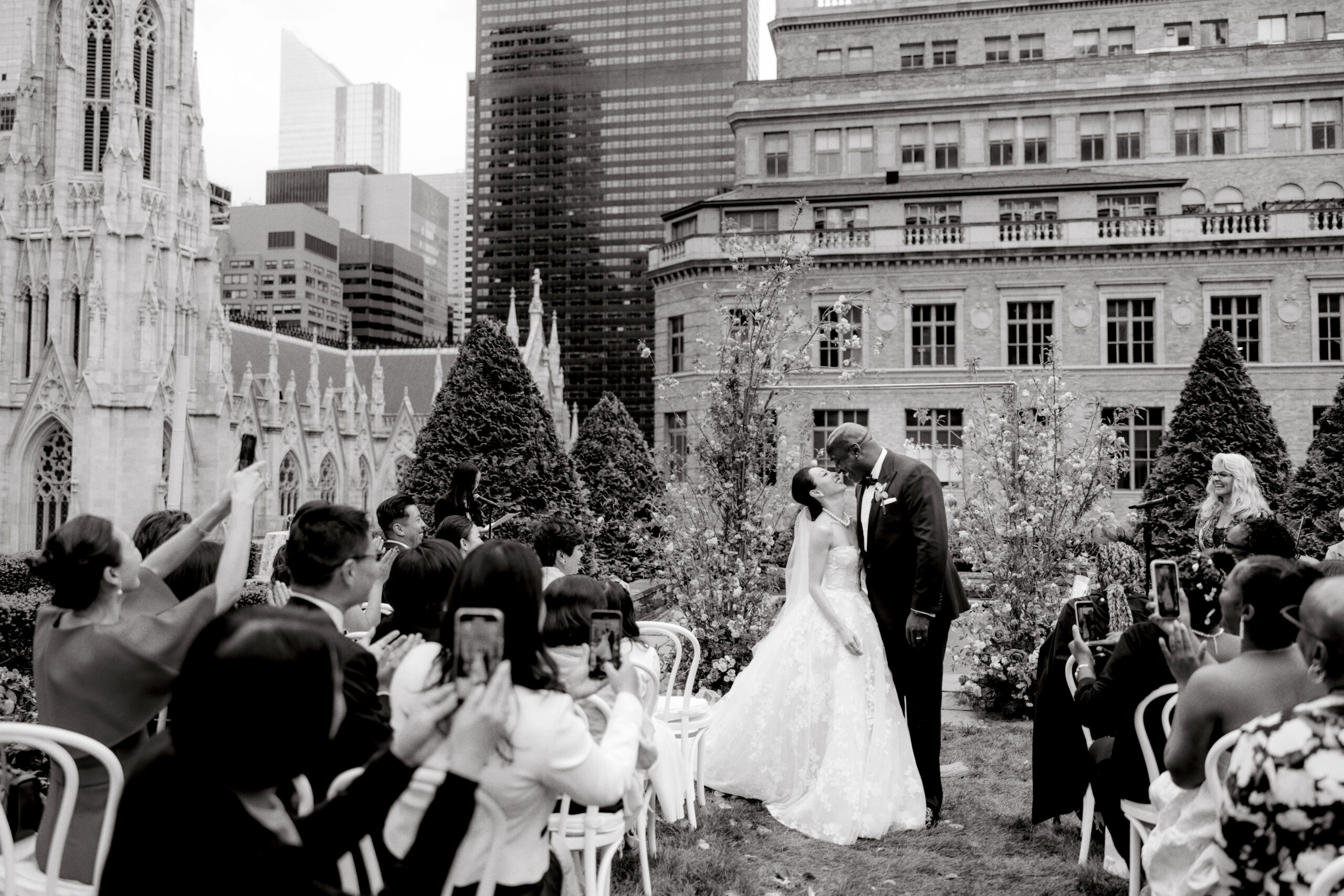 Black and white image of the newly-weds kissing at the wedding ceremony with St. Patrick's Cathedral in the background. Image by Jenny Fu Studio
