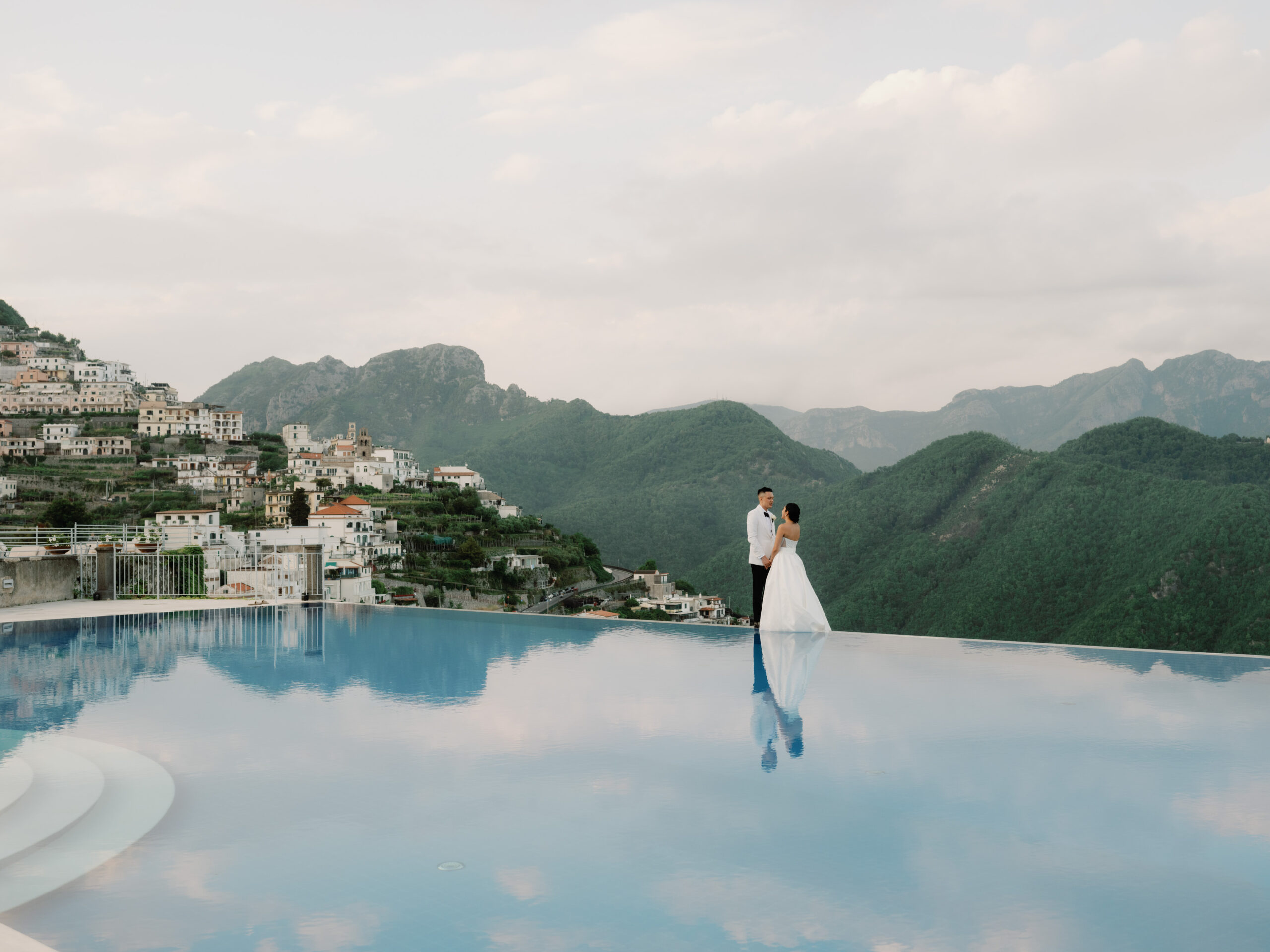 The newlyweds are standing in the infinity pool at Hotel Caruso Belmond, Italy. Image by Jenny Fu Studio