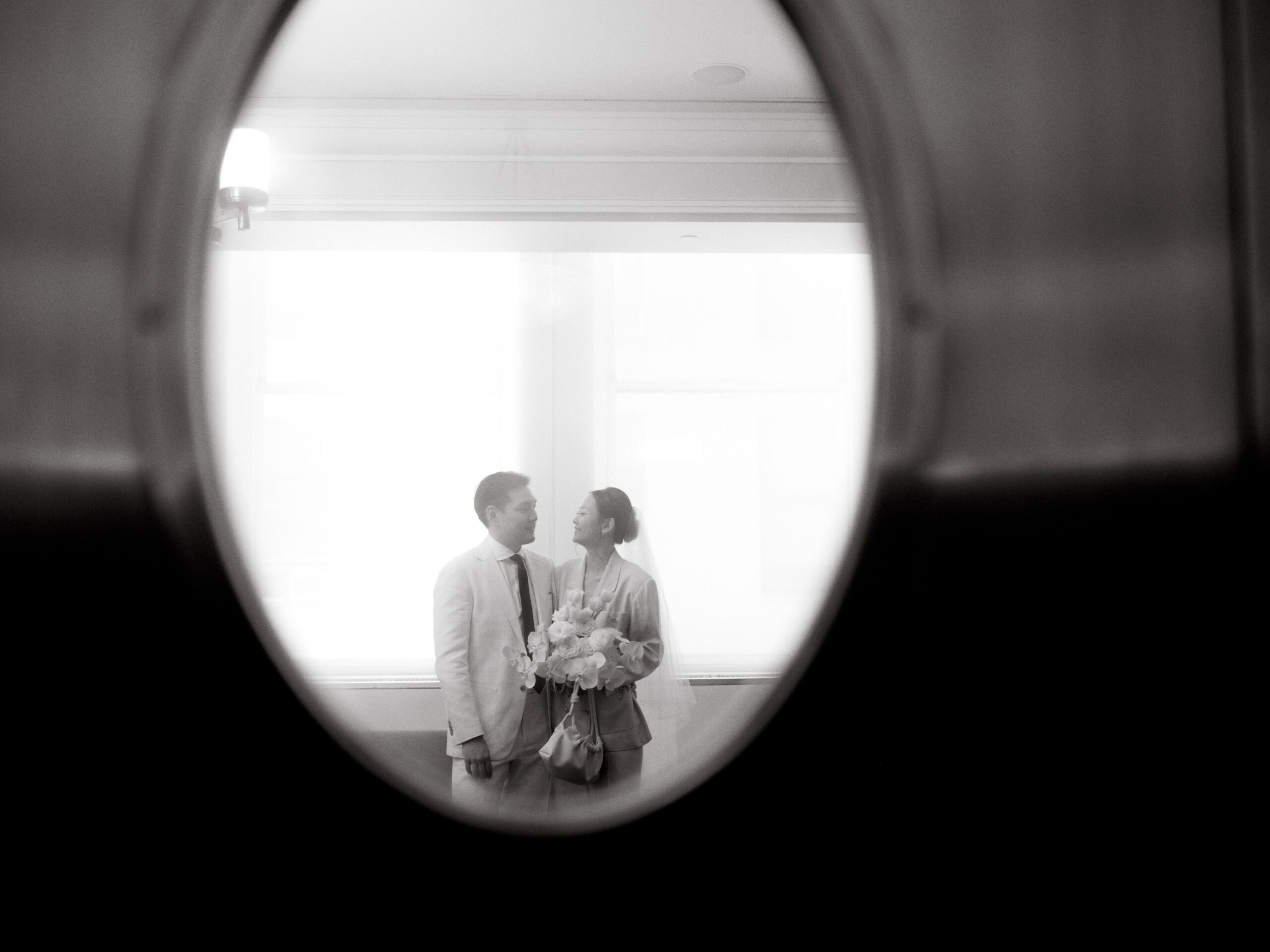 Black and white image of the bride and groom through the door window. Documentary Wedding Photography Image by Jenny Fu Studio
