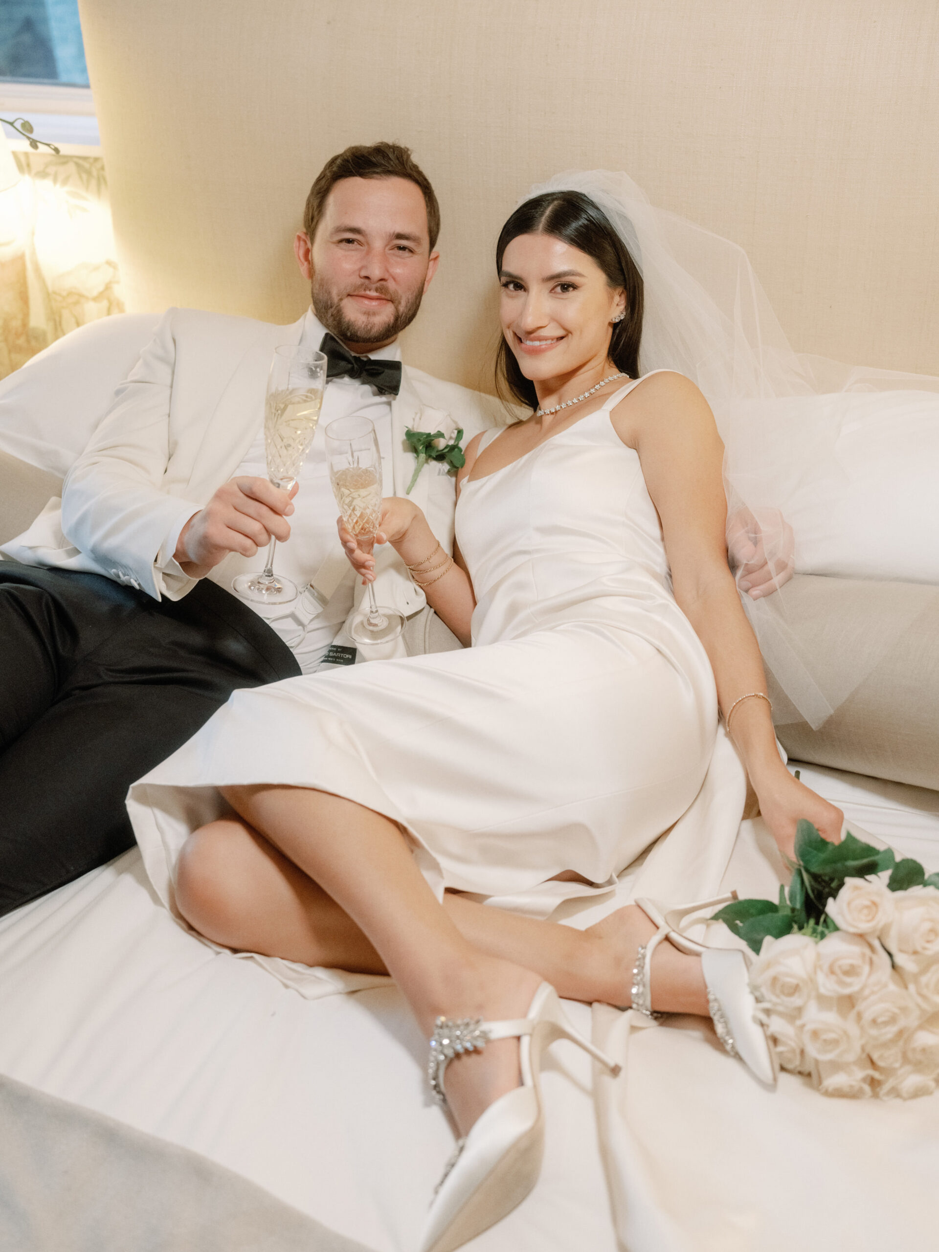 The newlyweds are lying on the bed, holding glasses of champagnes. Timeless Wedding Photography image by Jenny Fu Studio