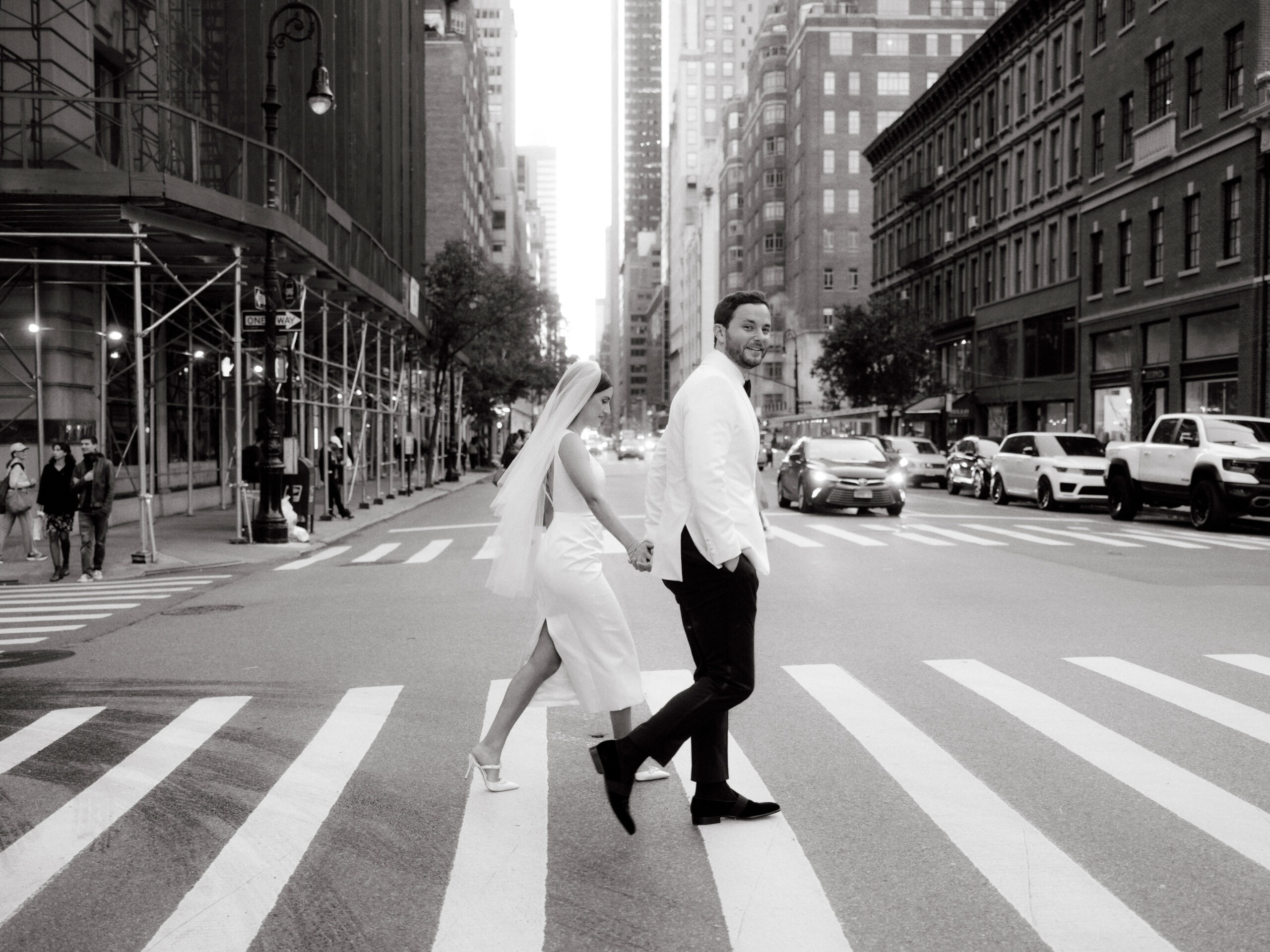 Black and white, candid photo of the newlyweds crossing a street in NYC. Timeless Wedding Photography by Jenny Fu Studio