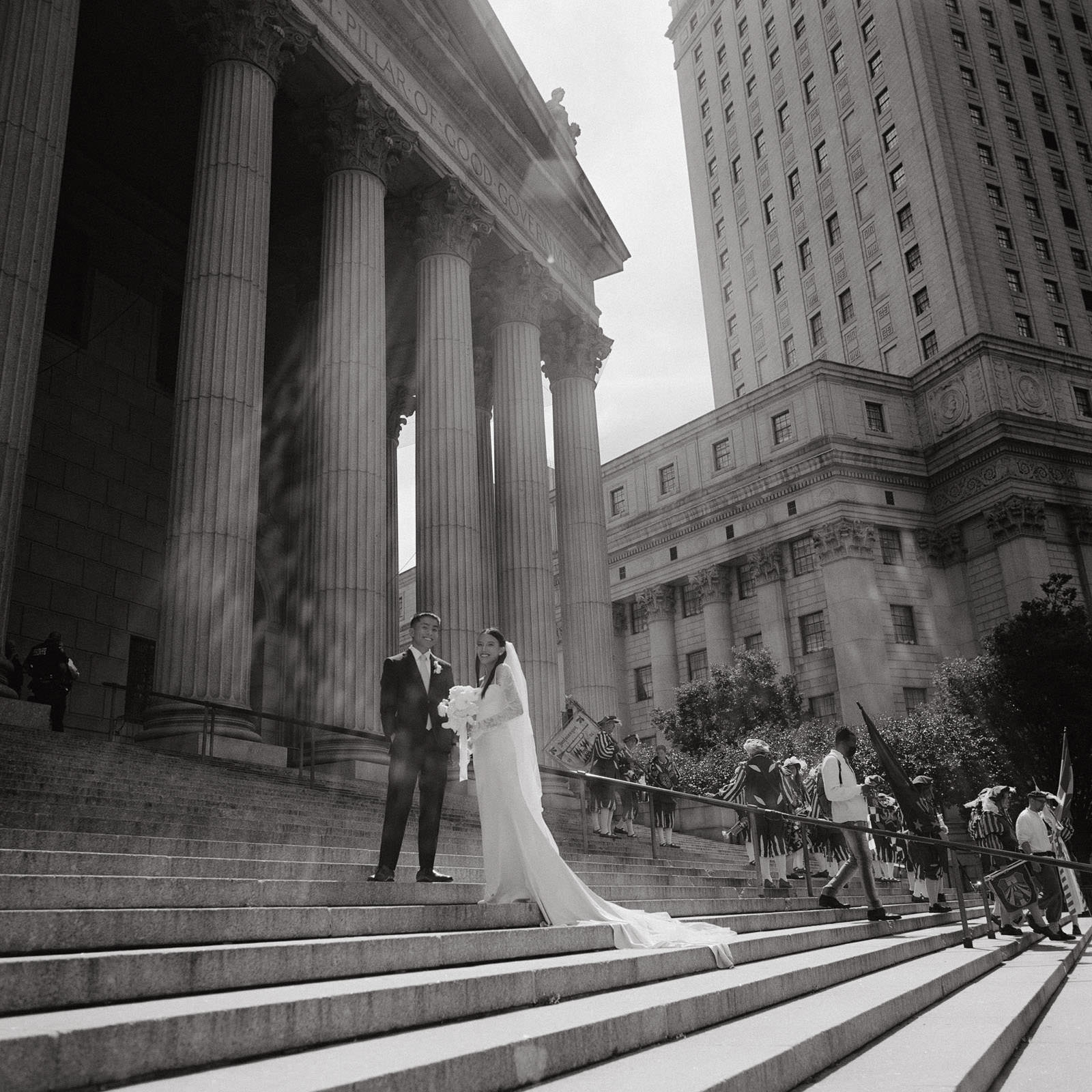 In the glow of a beautiful sunny afternoon, this captivating image captures a newly married couple basking in the warmth of their love at New York City Hall. The sun, a gentle artist, bestows its gleaming touch upon their union, casting a luminous aura that mirrors the radiance of their shared journey.