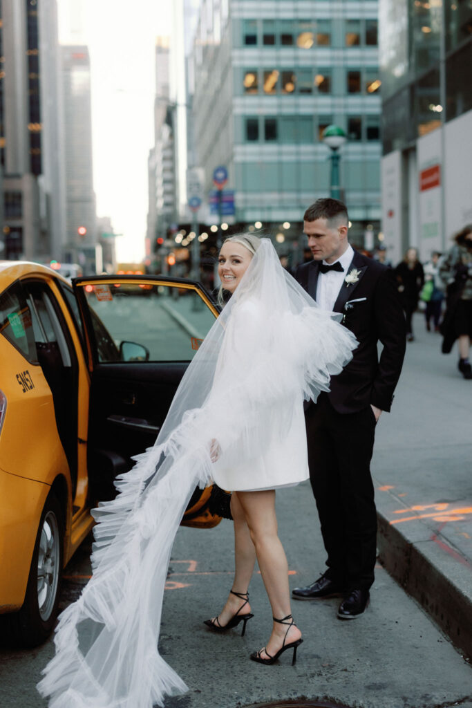 Amidst the bustling charm of Midtown, near the iconic New York Public Library, a bride and groom embark on a stylish getaway. Captured in this candid moment, the newlyweds step into a classic NYC taxi cab, their journey unfolding against the backdrop of the city's vibrant energy.

The bride's gown and the groom's attire, elegantly worn after their elopement ceremony, blend seamlessly with the urban tableau. As they settle into the taxi, the city becomes a romantic blur outside the window, framing this escape as a timeless snapshot in the heart of Manhattan.