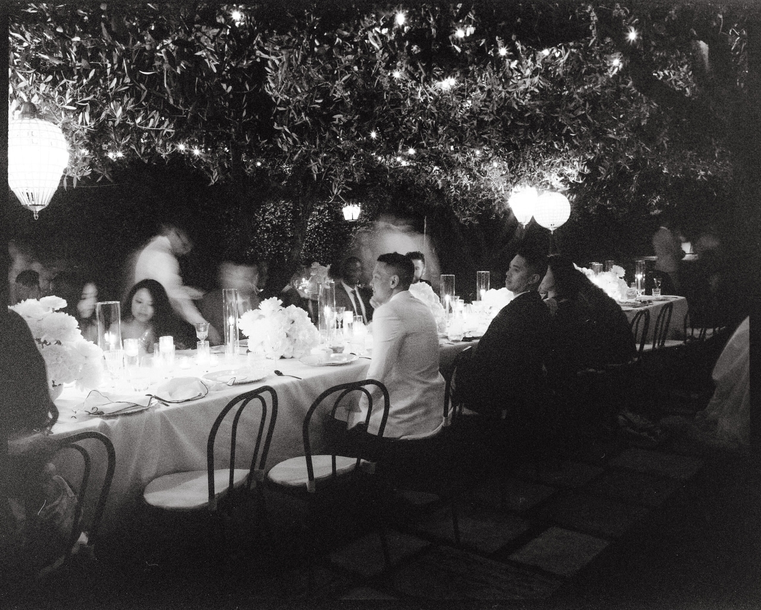 Groom immersed in joy during the summer dinner reception of a destination wedding in Ravello, Italy. Guests mingle in the warm ambiance of the celebration. This timeless moment, captured by Jenny Fu on film with a Mamiya 7 medium format camera, exudes classic elegance in black and white.

