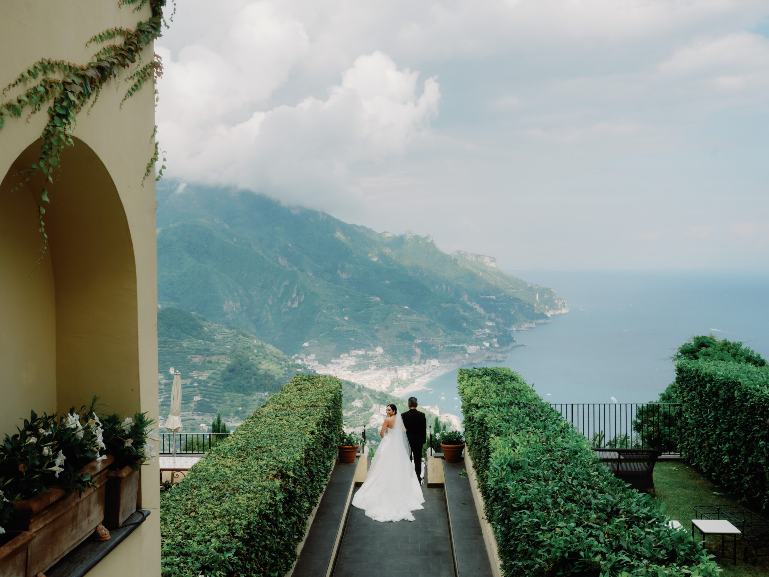 Breathtaking moment as the bride walks down to her wedding ceremony in Ravello, Italy, overlooking the stunning Amalfi Coast. The majestic backdrop features the iconic Caruso, a Belmond Hotel, creating a picture-perfect scene for this unforgettable day.