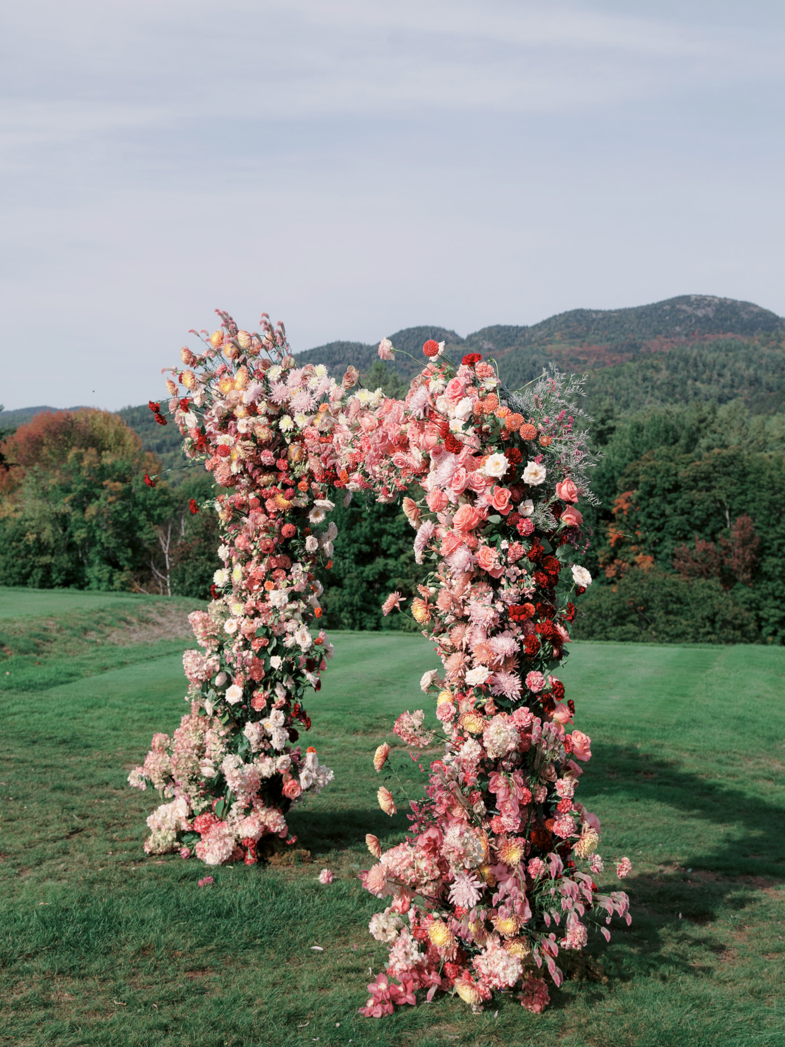 a lovely wedding arch overflowing with vibrant flowers amidst the Adirondack mountains in New York.