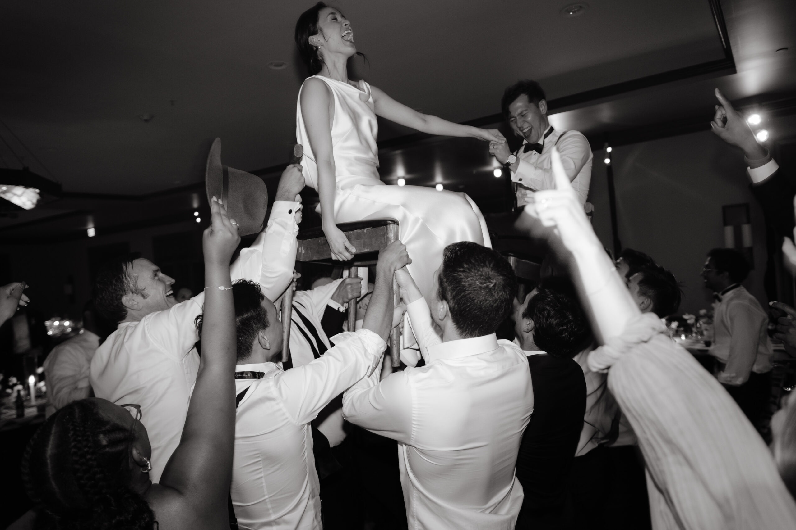 The bride and groom are exhilarated, sitting on a chair while being carried high up in the air. Image by Jenny Fu Studio