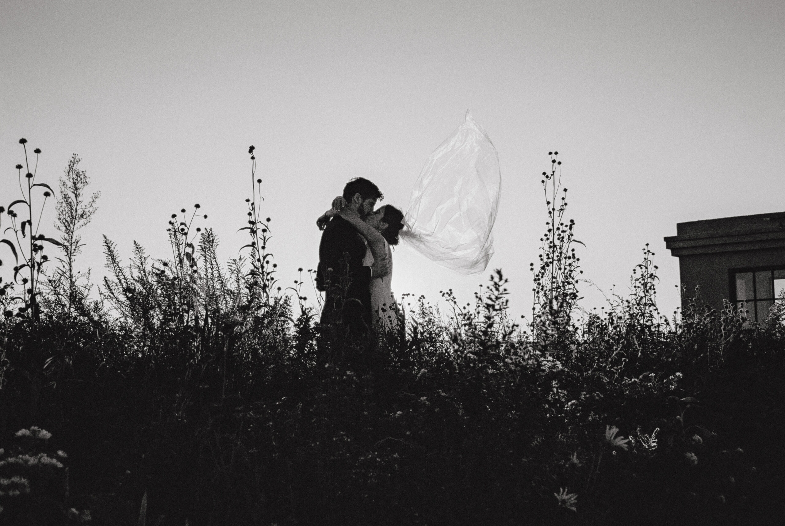 Black and white editorial image of the bride and groom kissing outdoors. Image by Jenny Fu Studio
