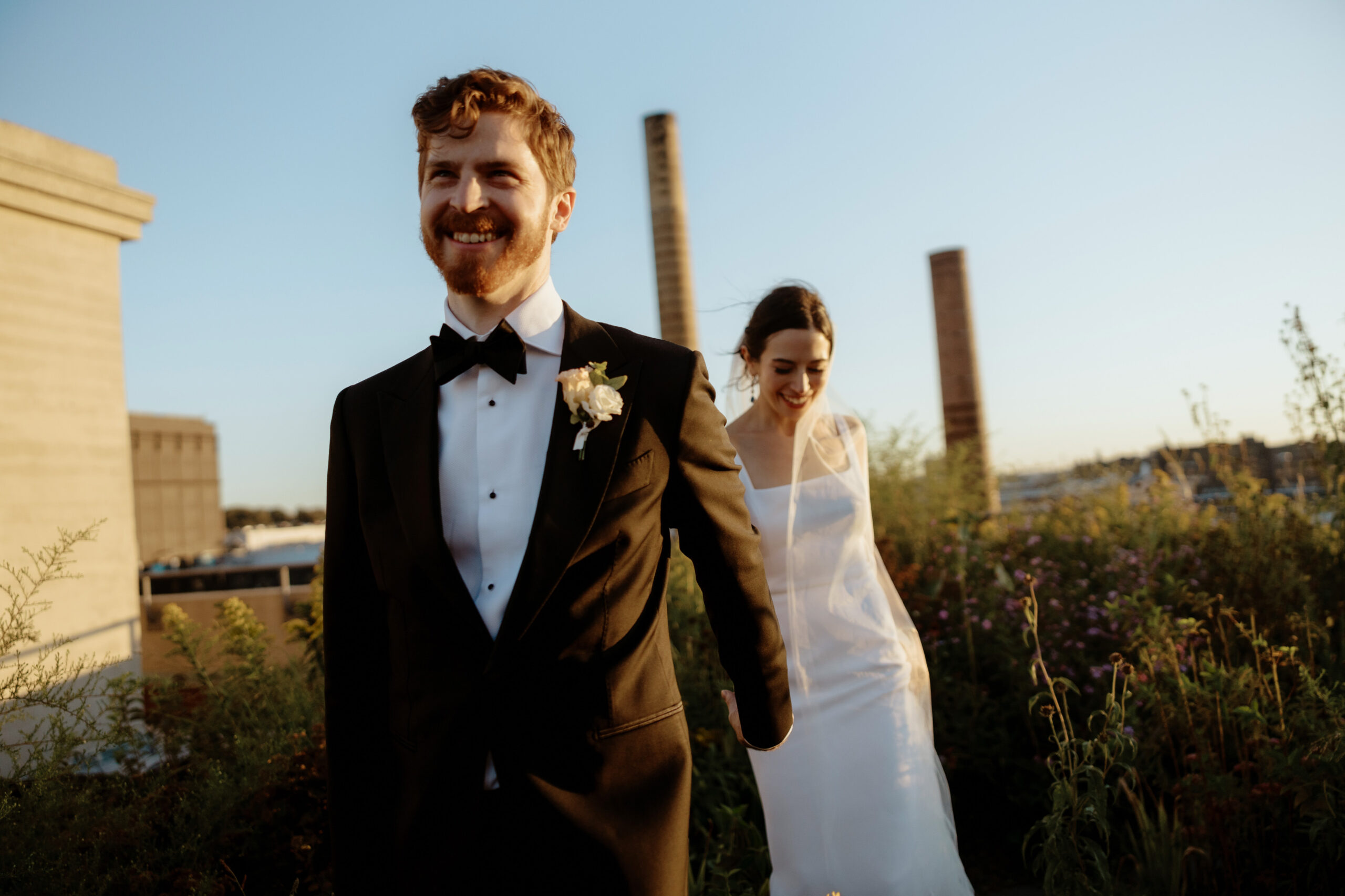 Documentary photo of the bride and groom happily walking hand in hand outdoors at The Brooklyn Grange. Image by Jenny Fu Studio