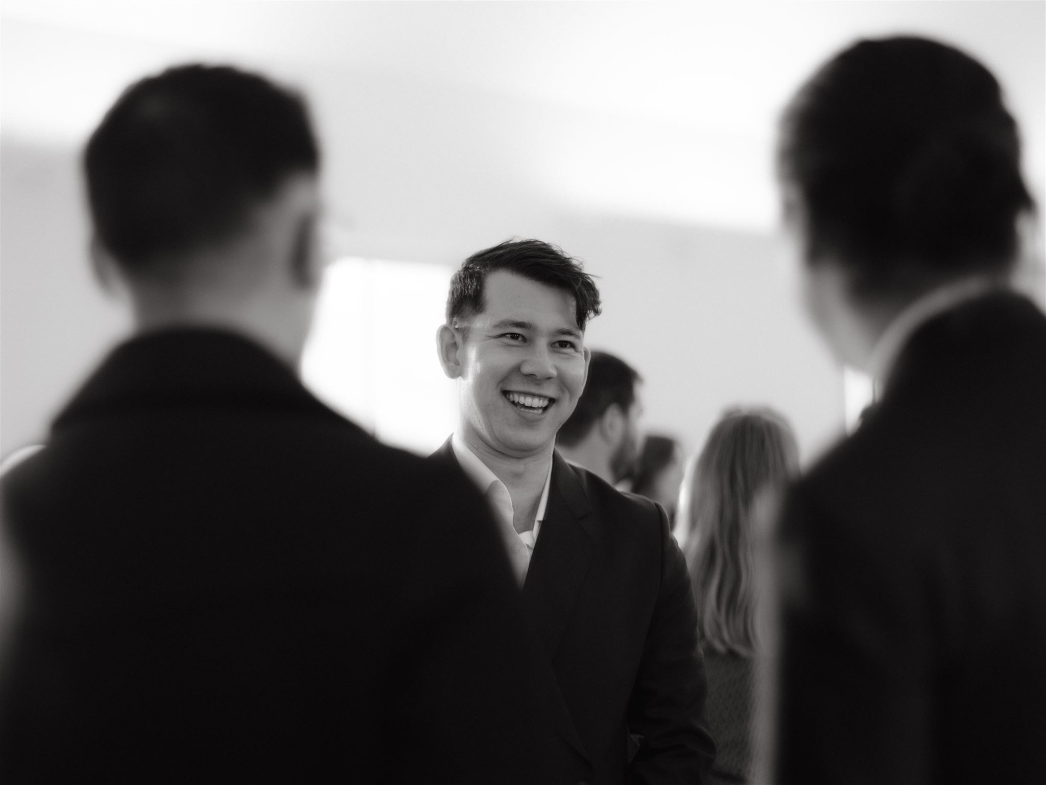 Black and white candid photo of the groom-to-be chatting with guests in their welcome dinner. Image by Jenny Fu Studio
