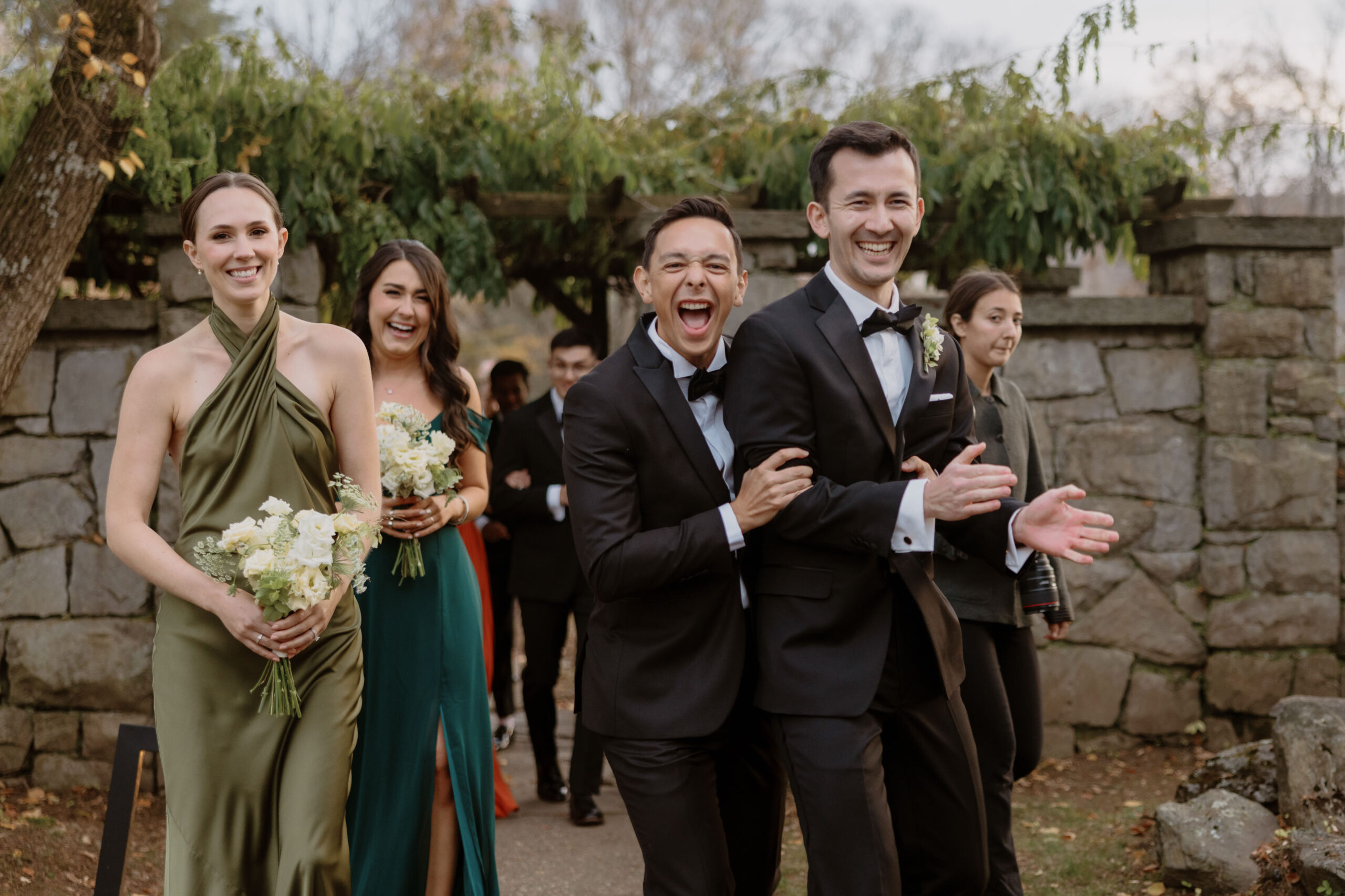 The bridesmaids and groomsmen smile at the camera while walking away after the wedding ceremony. Image by Jenny Fu Studio