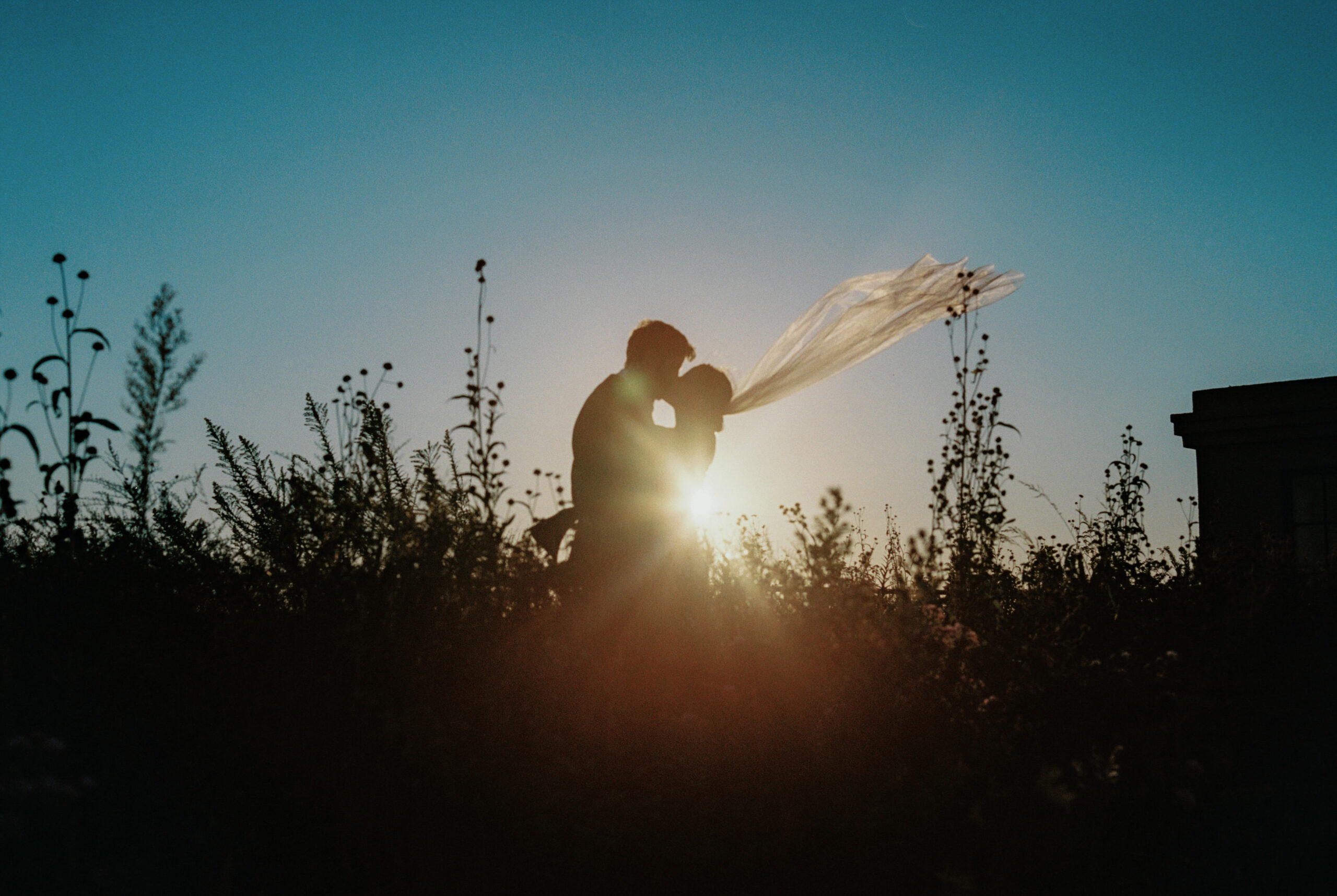 The bride and groom are kissing outdoors with sunset in the background. Image by Jenny Fu Studio