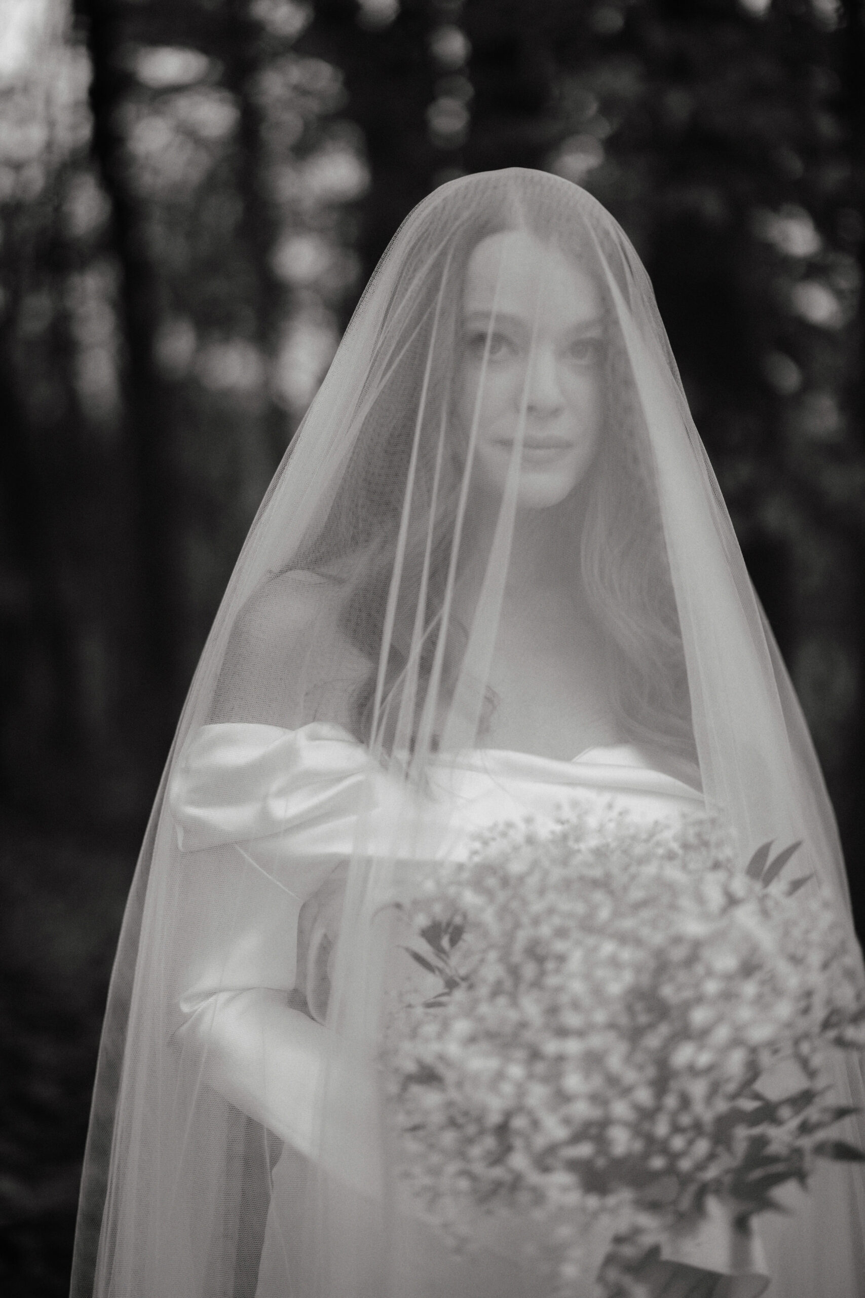 Black and white portrait of the bride holding her flower bouquet, wearing her veil. Image by Jenny Fu Studio