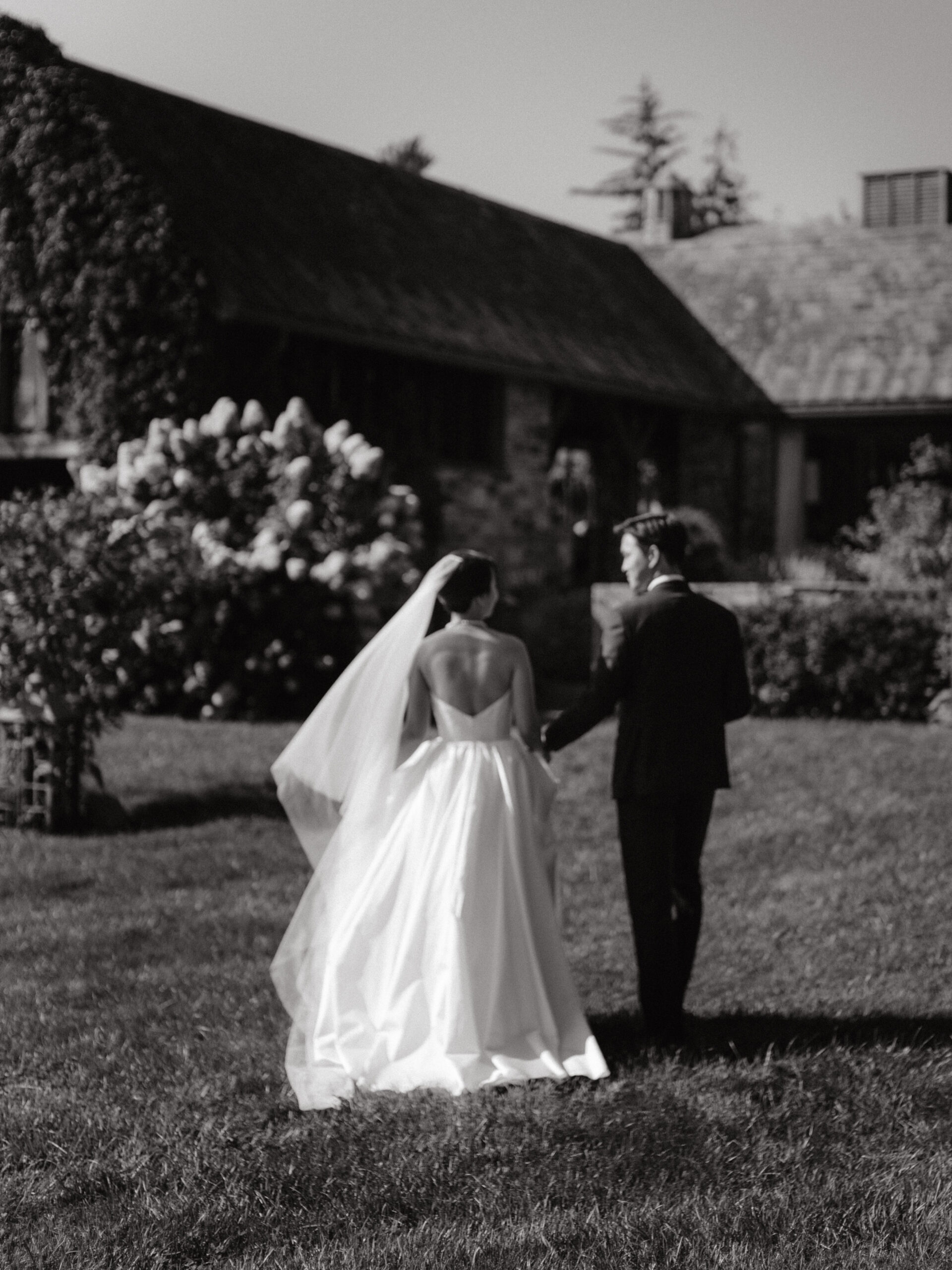 Black and white documentary wedding photography image of the bride and groom walking towards outdoors. Image by Jenny Fu Studio