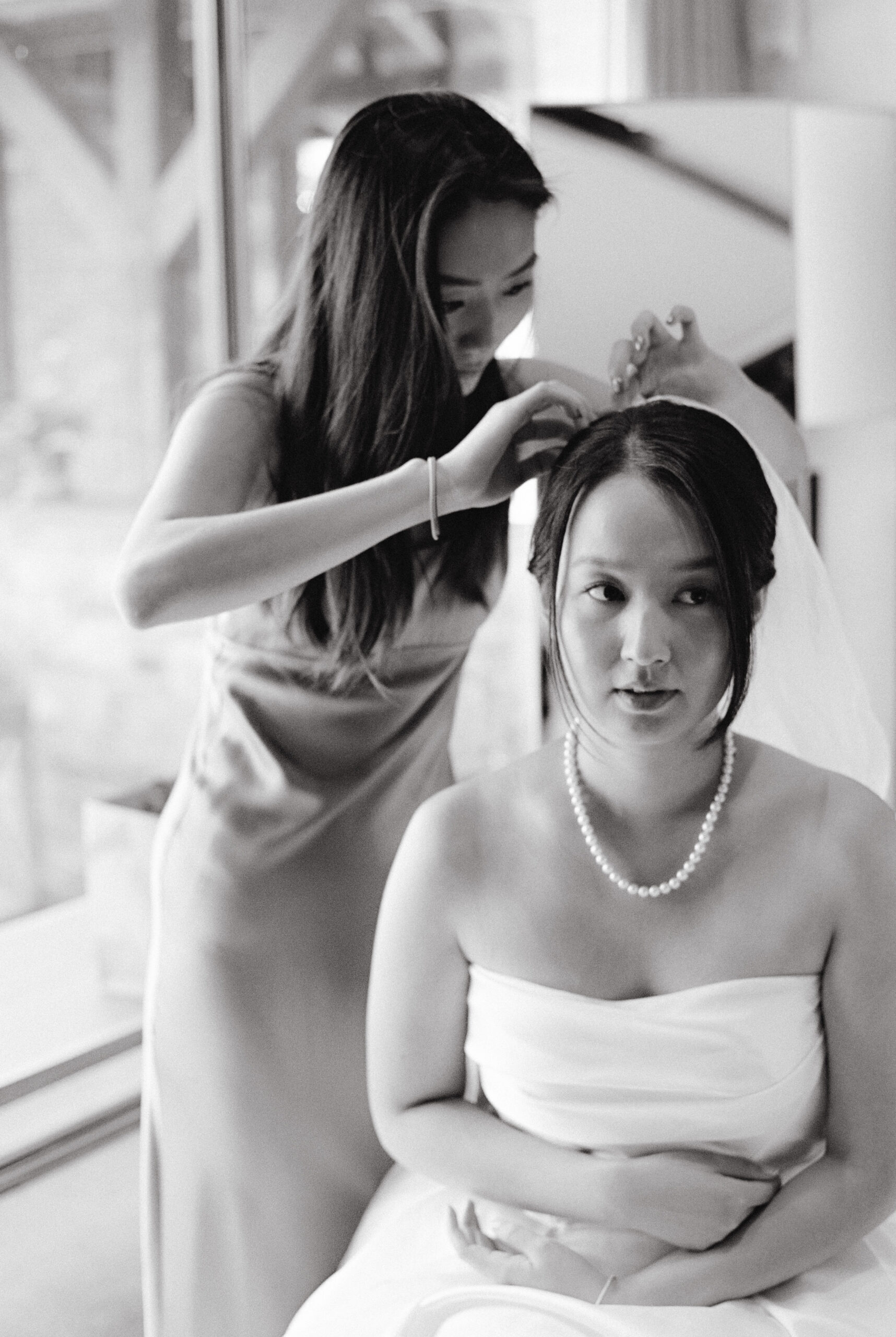 A bridesmaid is fixing the bride's hair and veil after the wedding ceremony. Photojournalistic image by Jenny Fu Studio