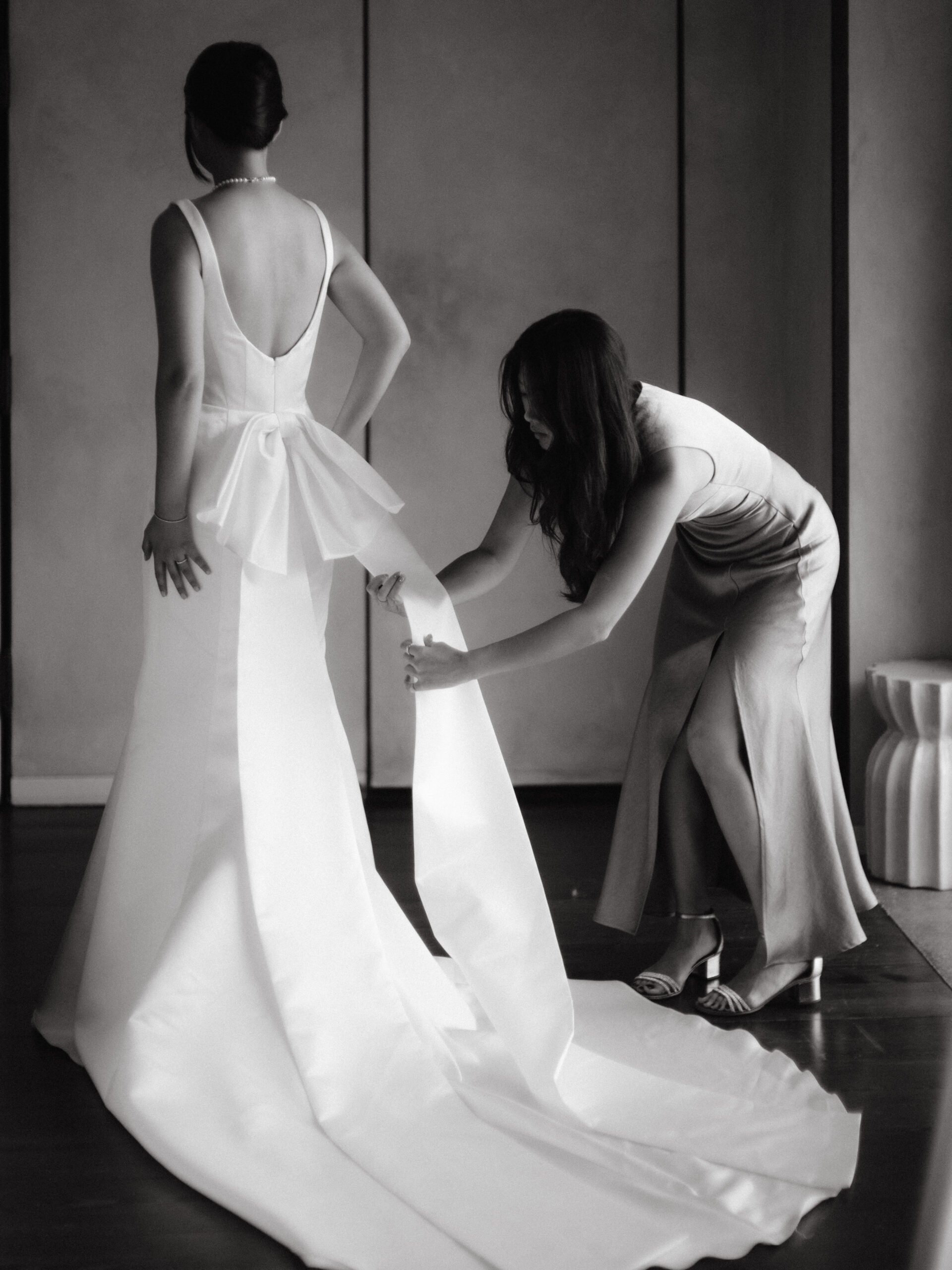 Black  and white image of the bridesmaid helping the bride change to her wedding reception dress. Image by Jenny Fu Studio
